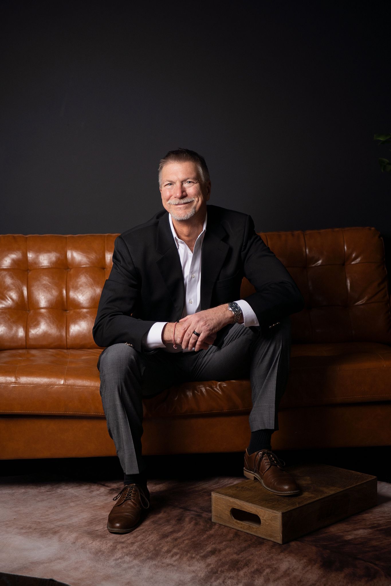 Professional portrait series showing a person in a dark suit seated on a brown leather couch in varying poses.