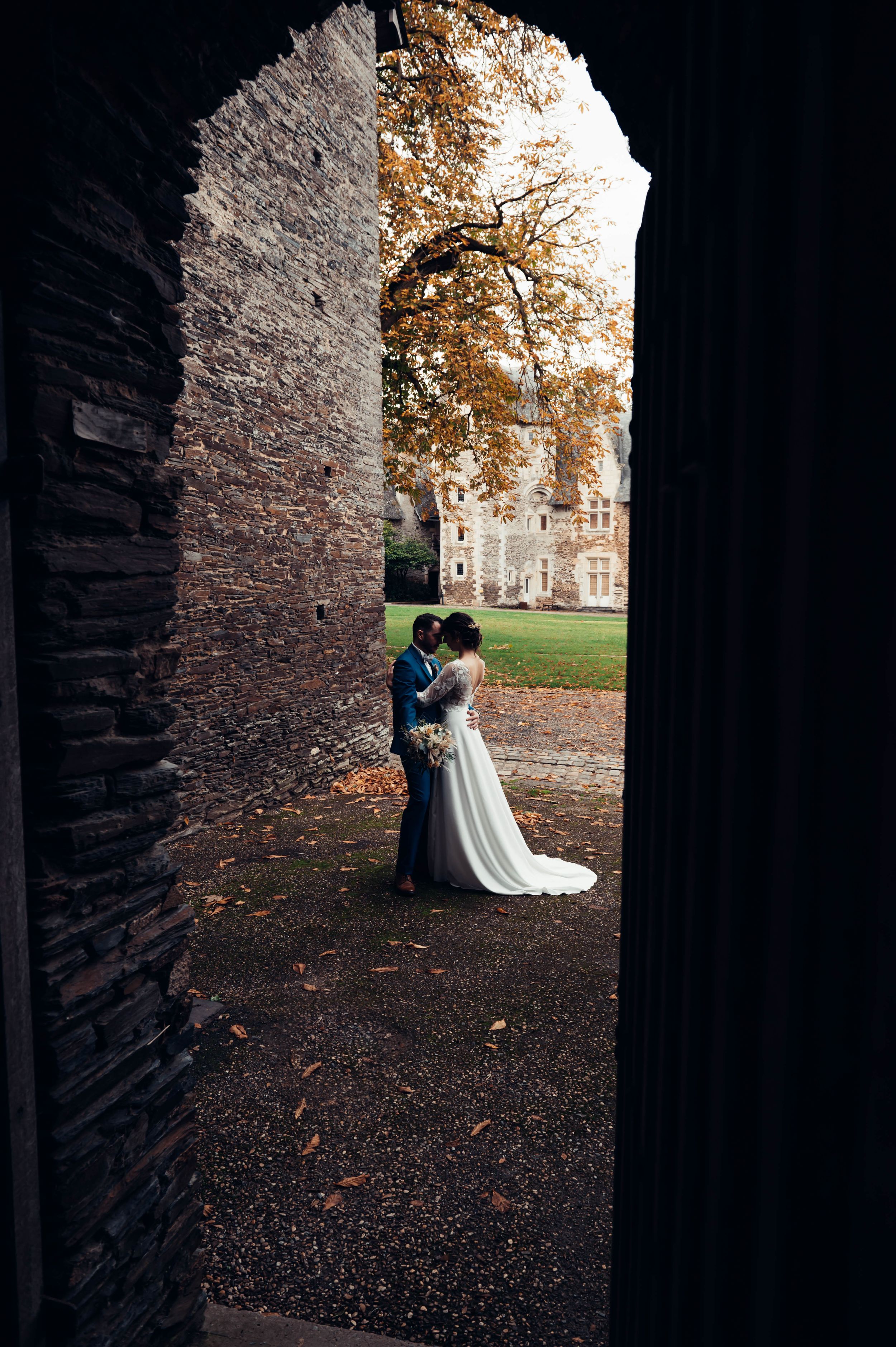 Mariée encadrée par une arche en pierre dans un lieu historique en Bretagne, photo de mariage naturelle.