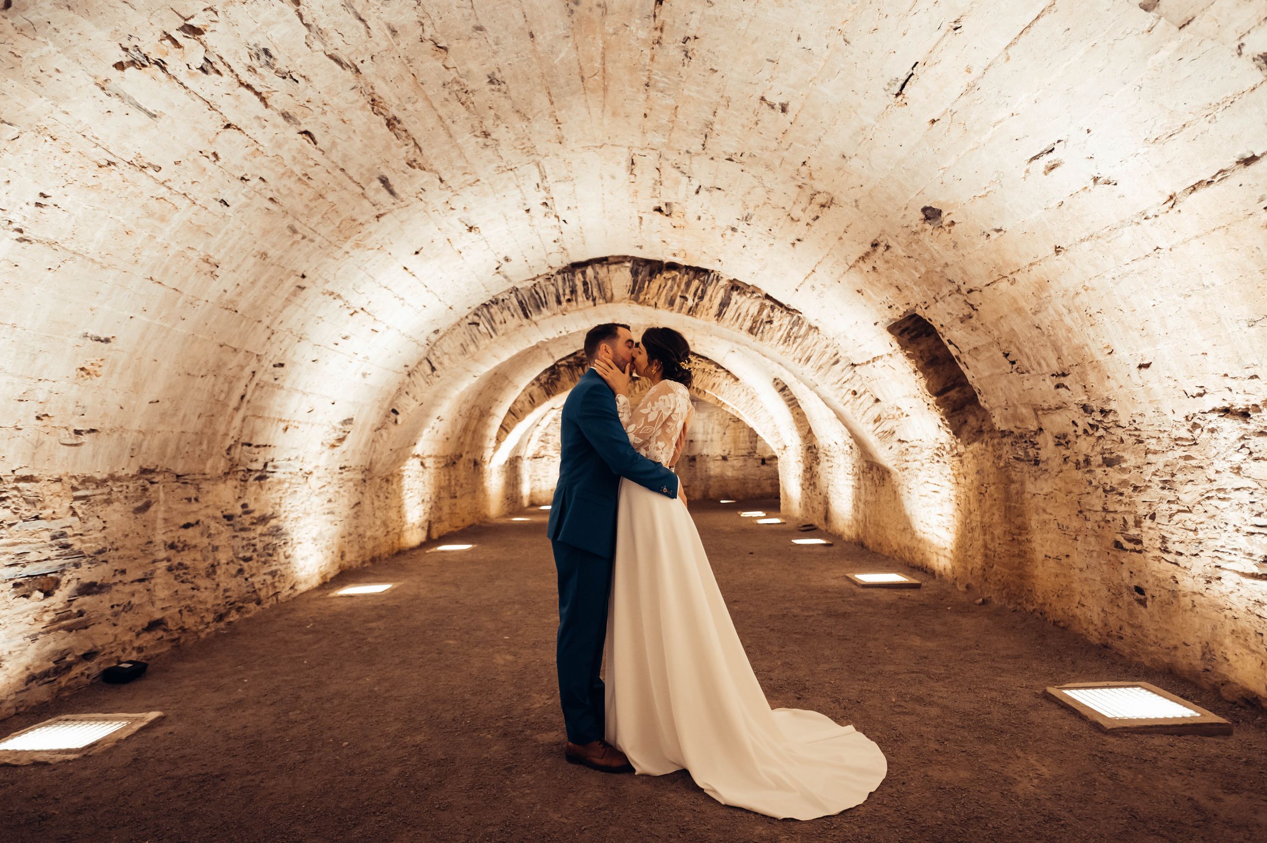 Couple de mariés enlacé sous une arche en pierre éclairée, séance photo de mariage en Bretagne.