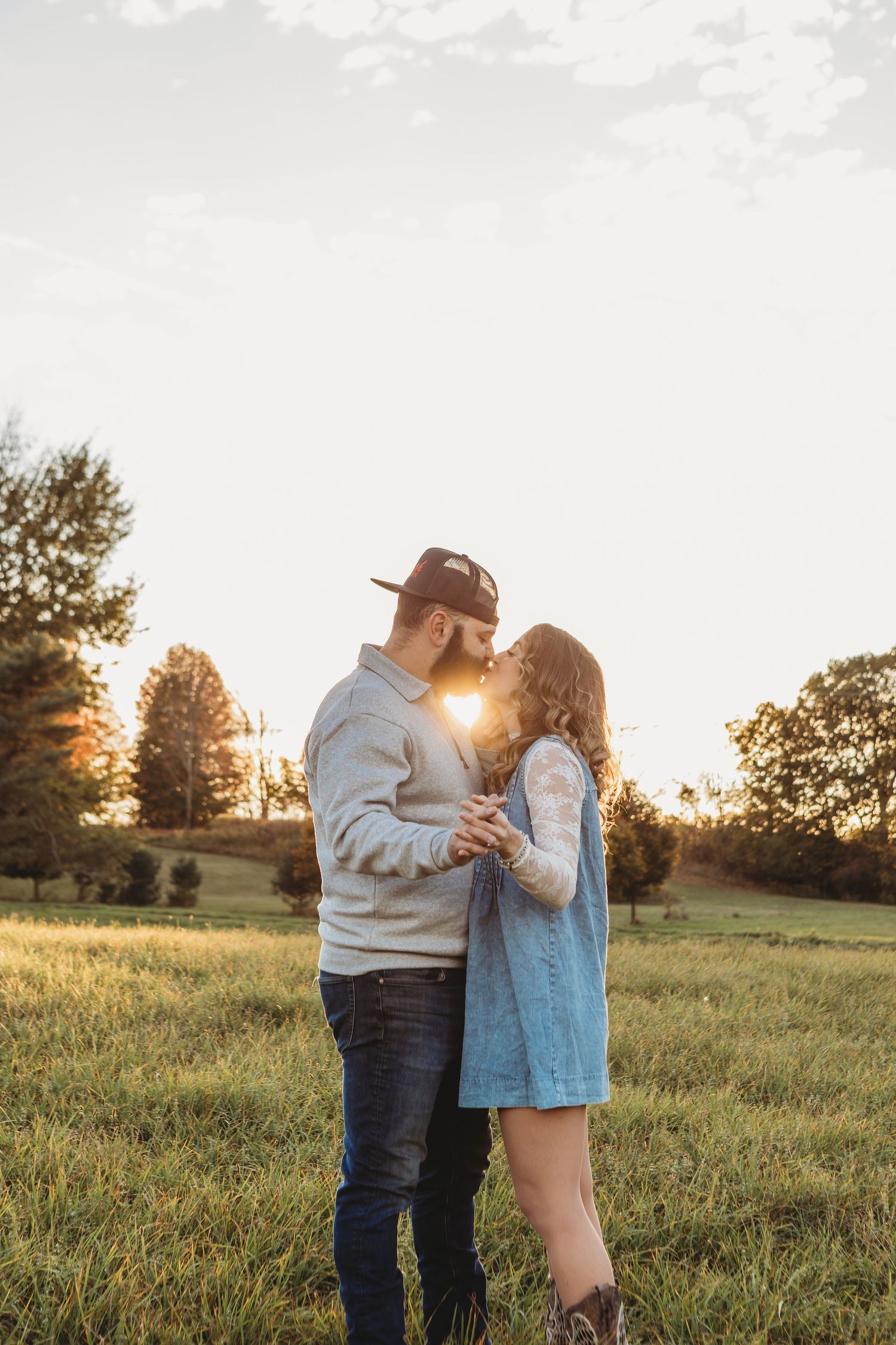 Romantic couple embracing in grassy field during golden sunset.