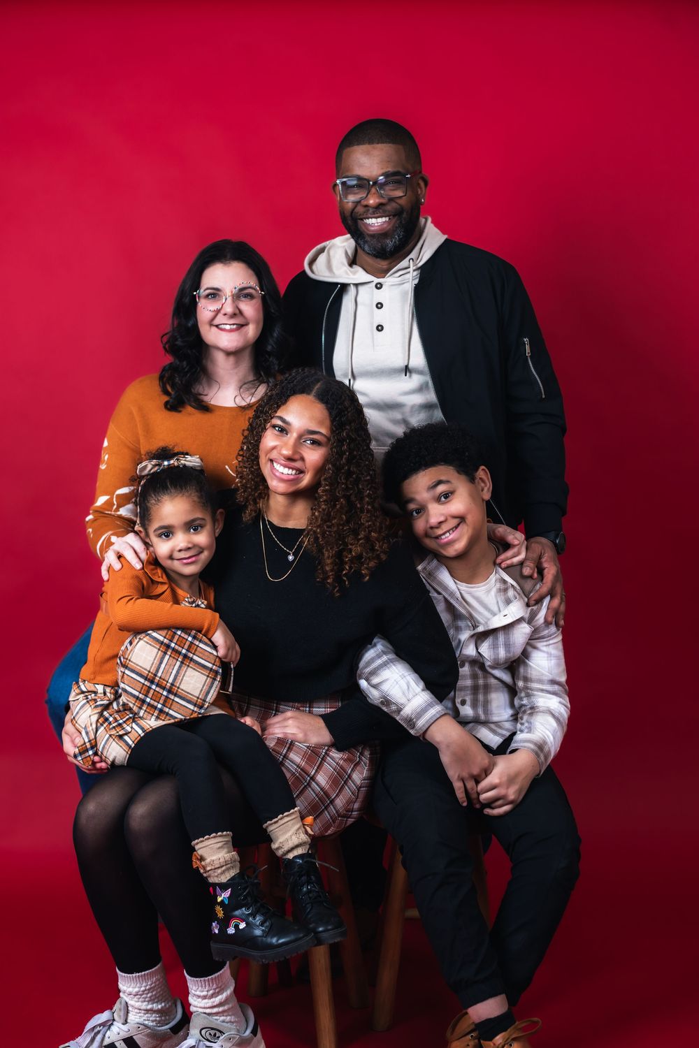 Family portrait session with red backdrop showing joyful expressions and coordinated casual outfits in multiple poses.