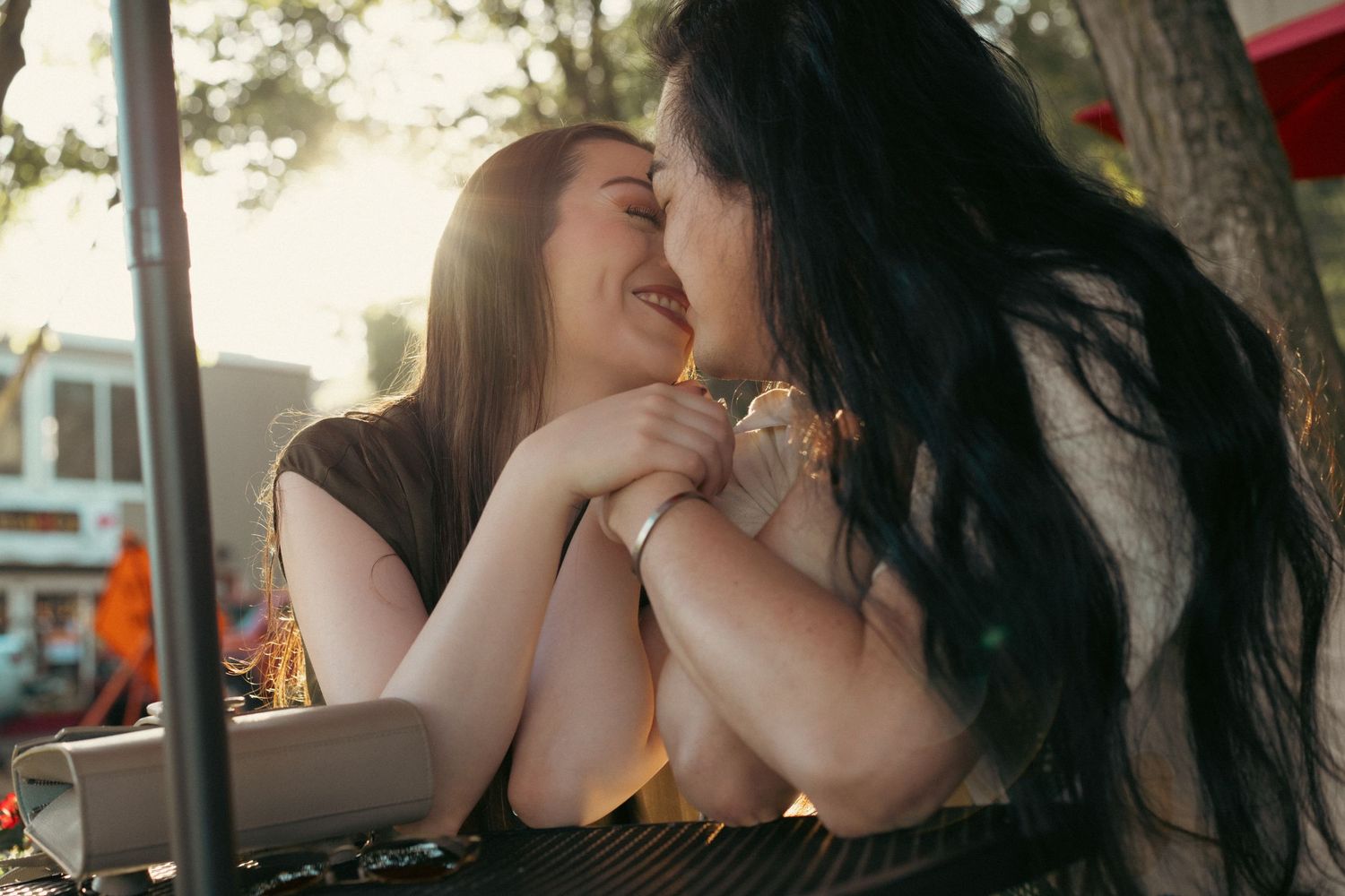 Two people share an intimate moment outdoors with sunlight filtering through trees in the background. captured by Savvy Photography
