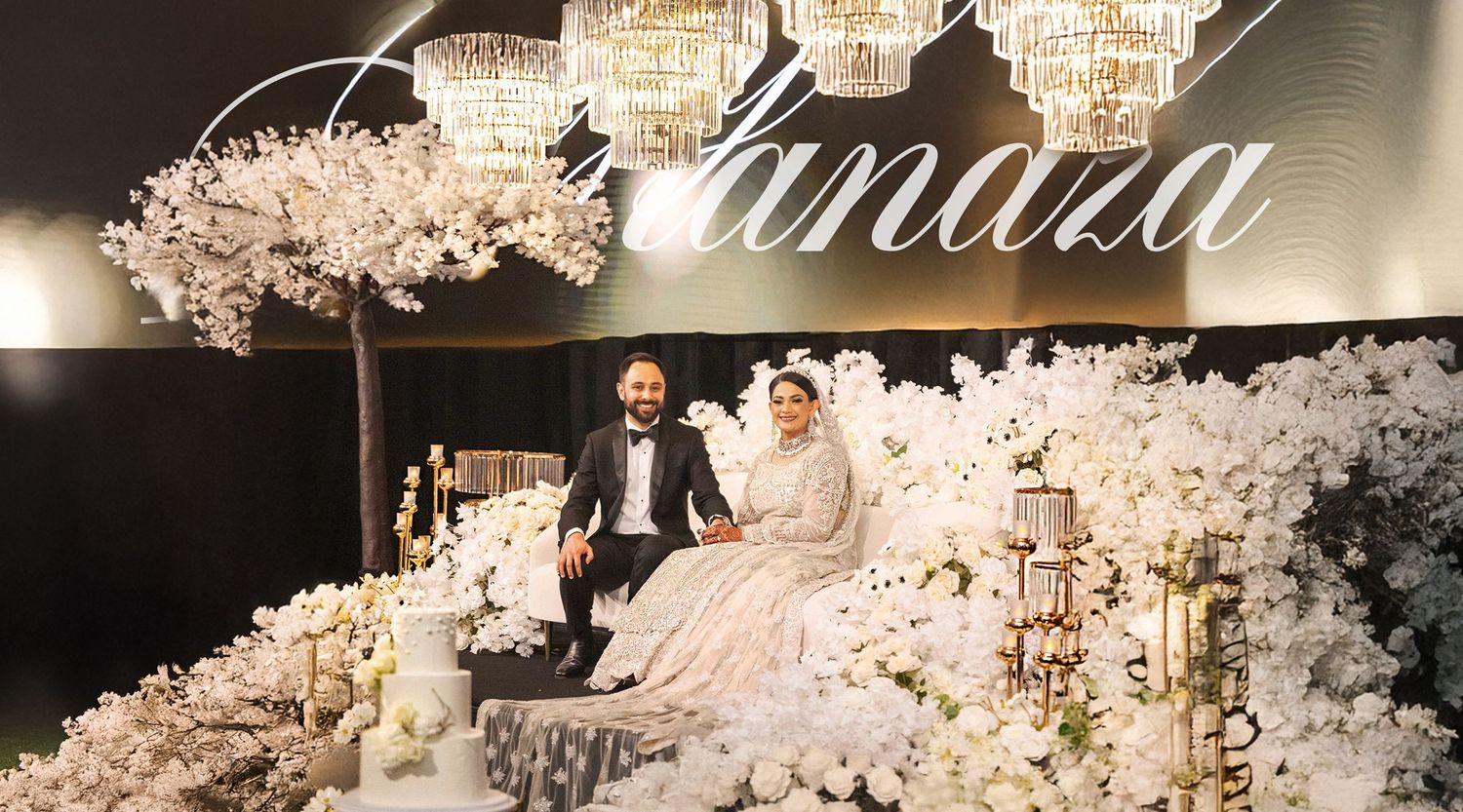 Bride and groom pose elegantly at decorated wedding reception under crystal chandeliers and white florals.