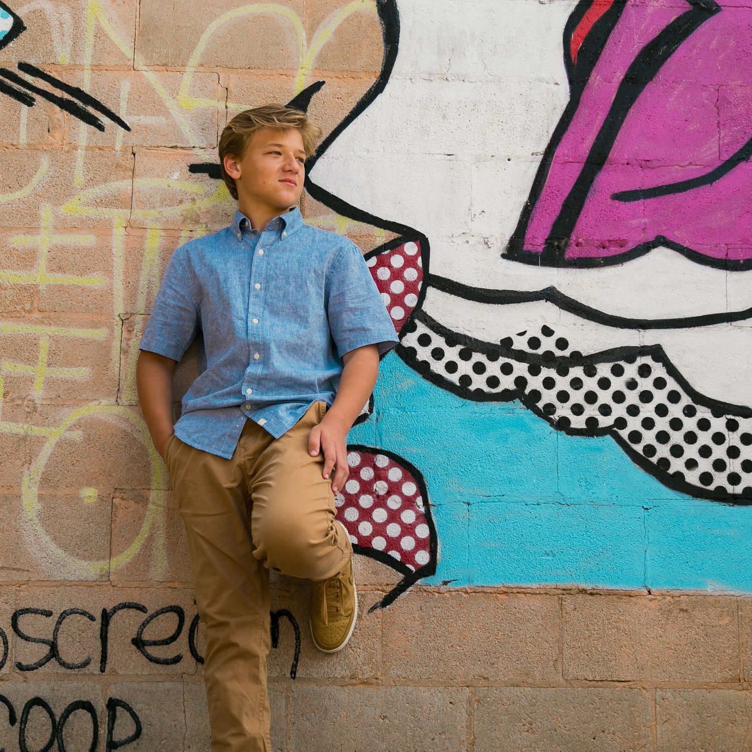 Person in casual attire posing against a colorful graffiti wall with geometric patterns.