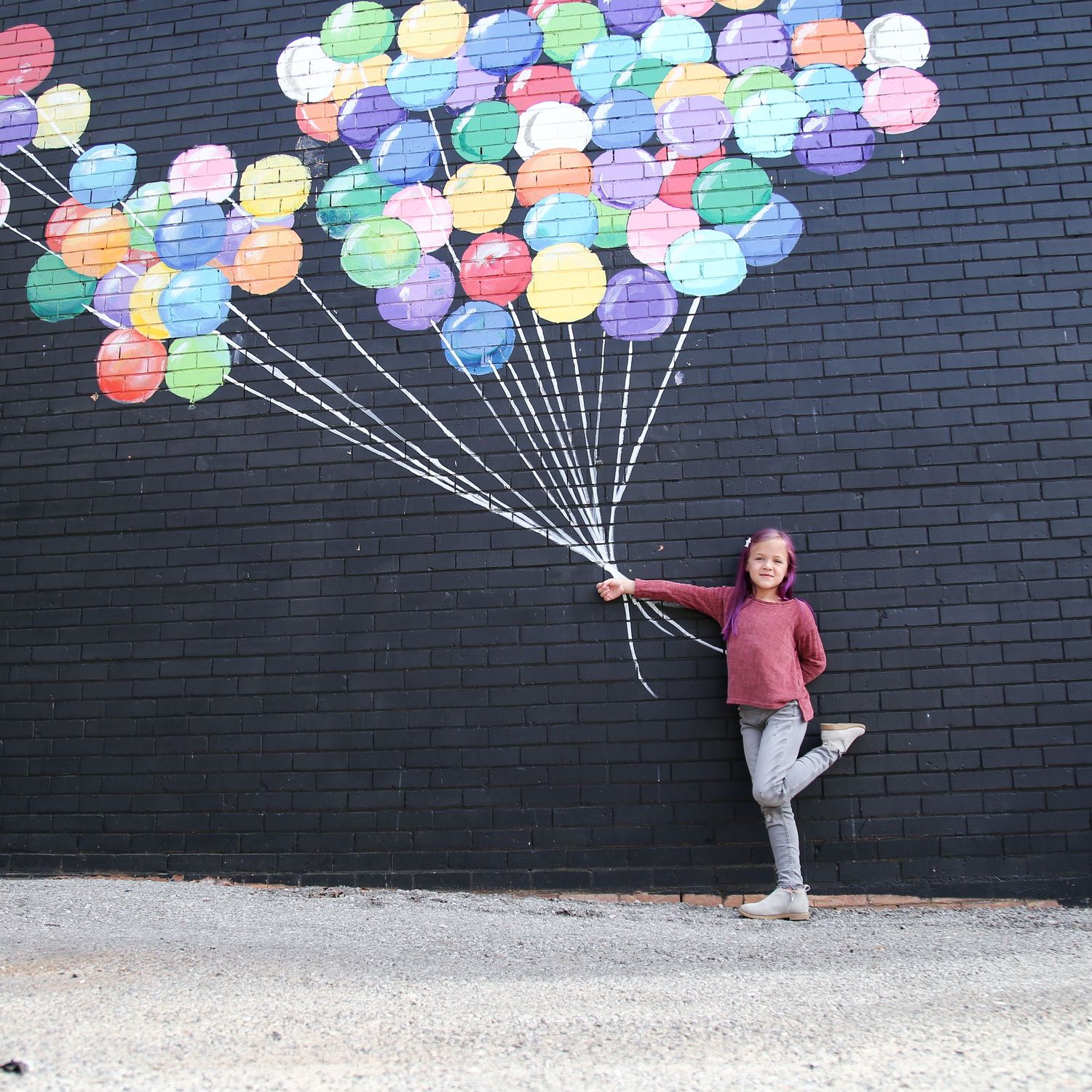 Colorful balloon mural on black brick wall with person posing playfully.