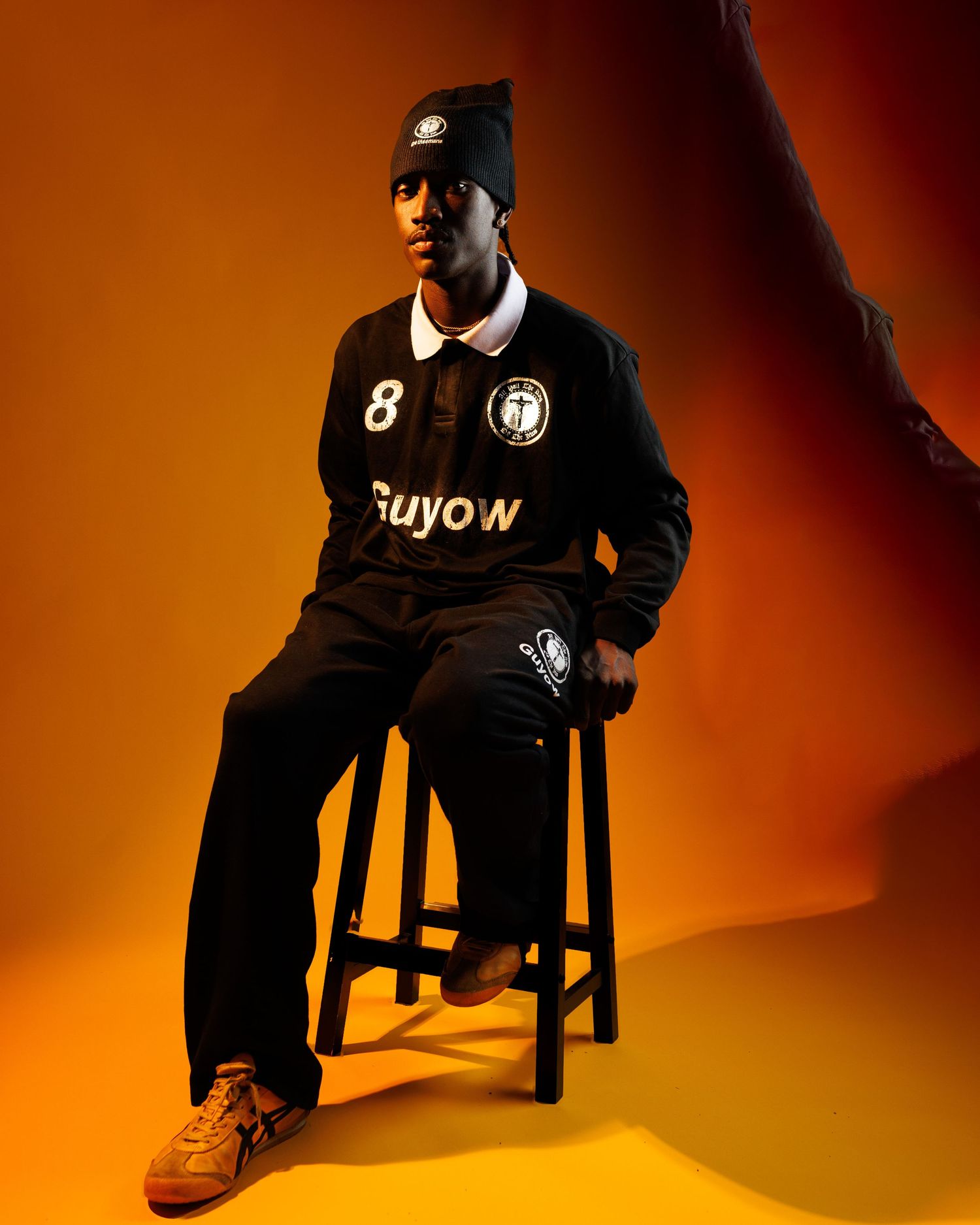 Basketball player in black uniform poses dramatically against orange and black gradient backdrop for professional photoshoot.