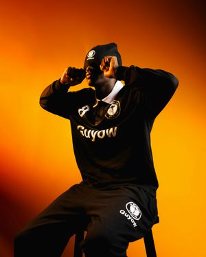 Silhouetted figure in black hoodie performs dramatic dance moves against vibrant orange background.