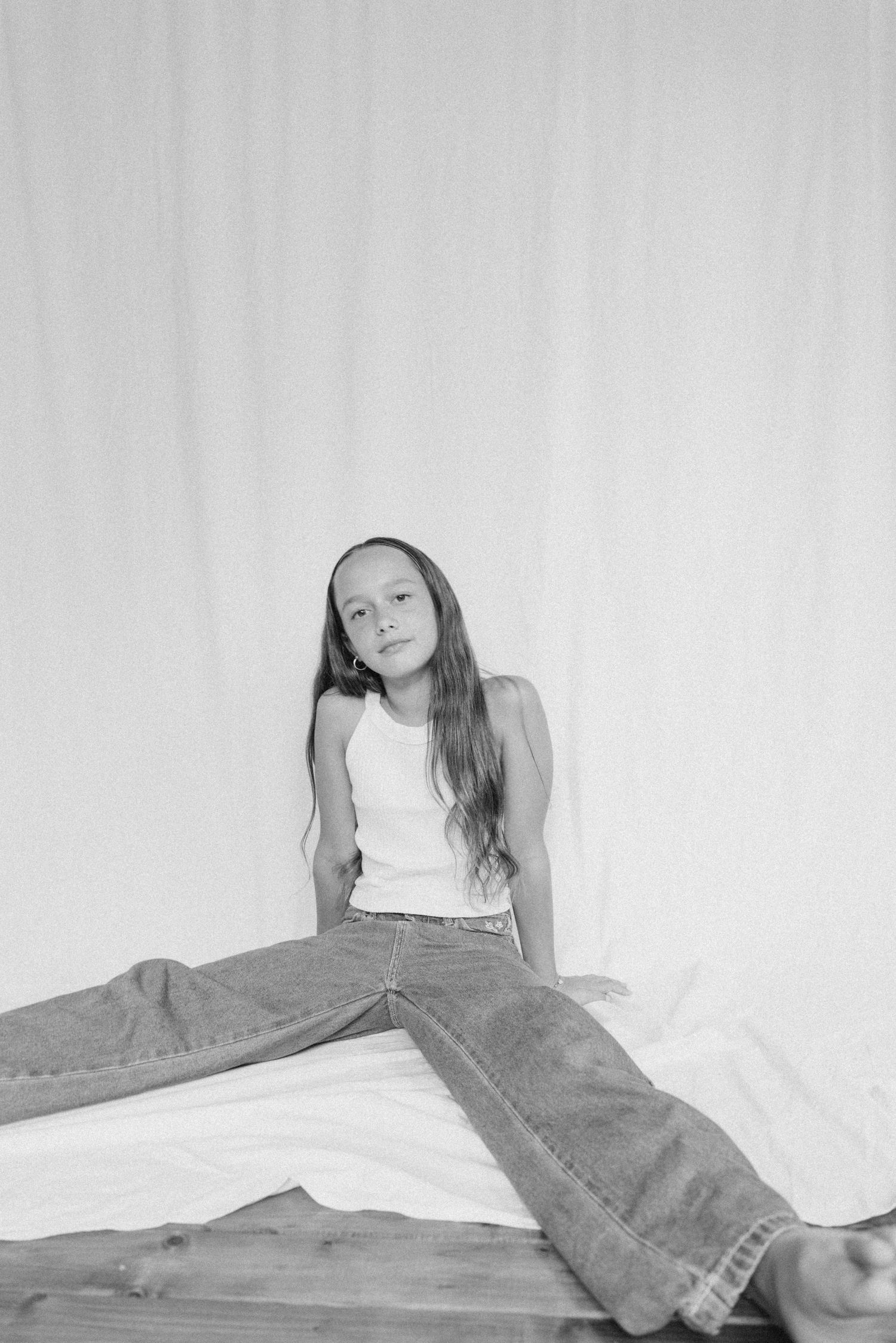 A young girl in a white tank top and jeans poses on a white backdrop in black and white in New Zealand.