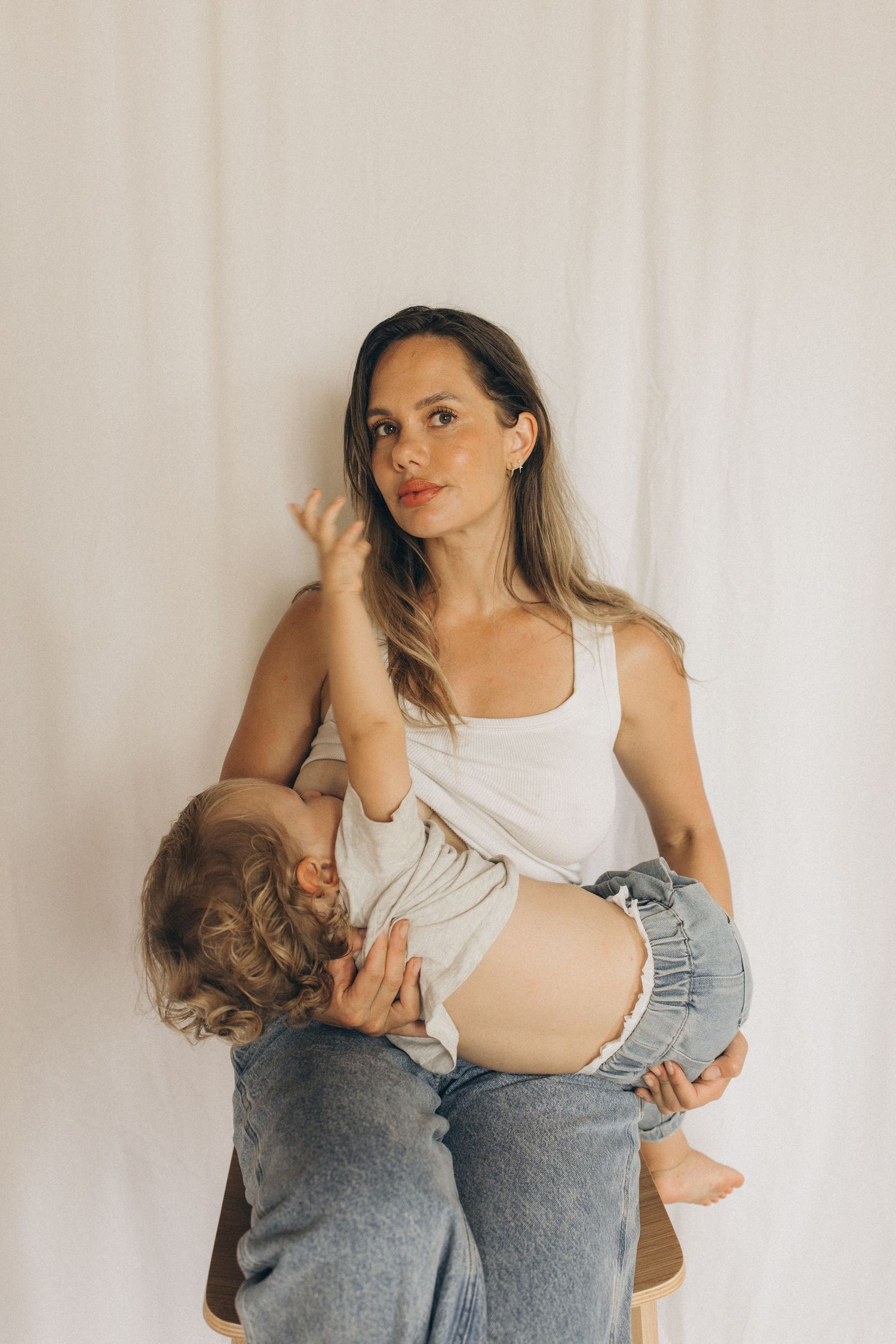 A mother in a white tank top and jeans holds her toddler during a studio photo session in New Zealand.