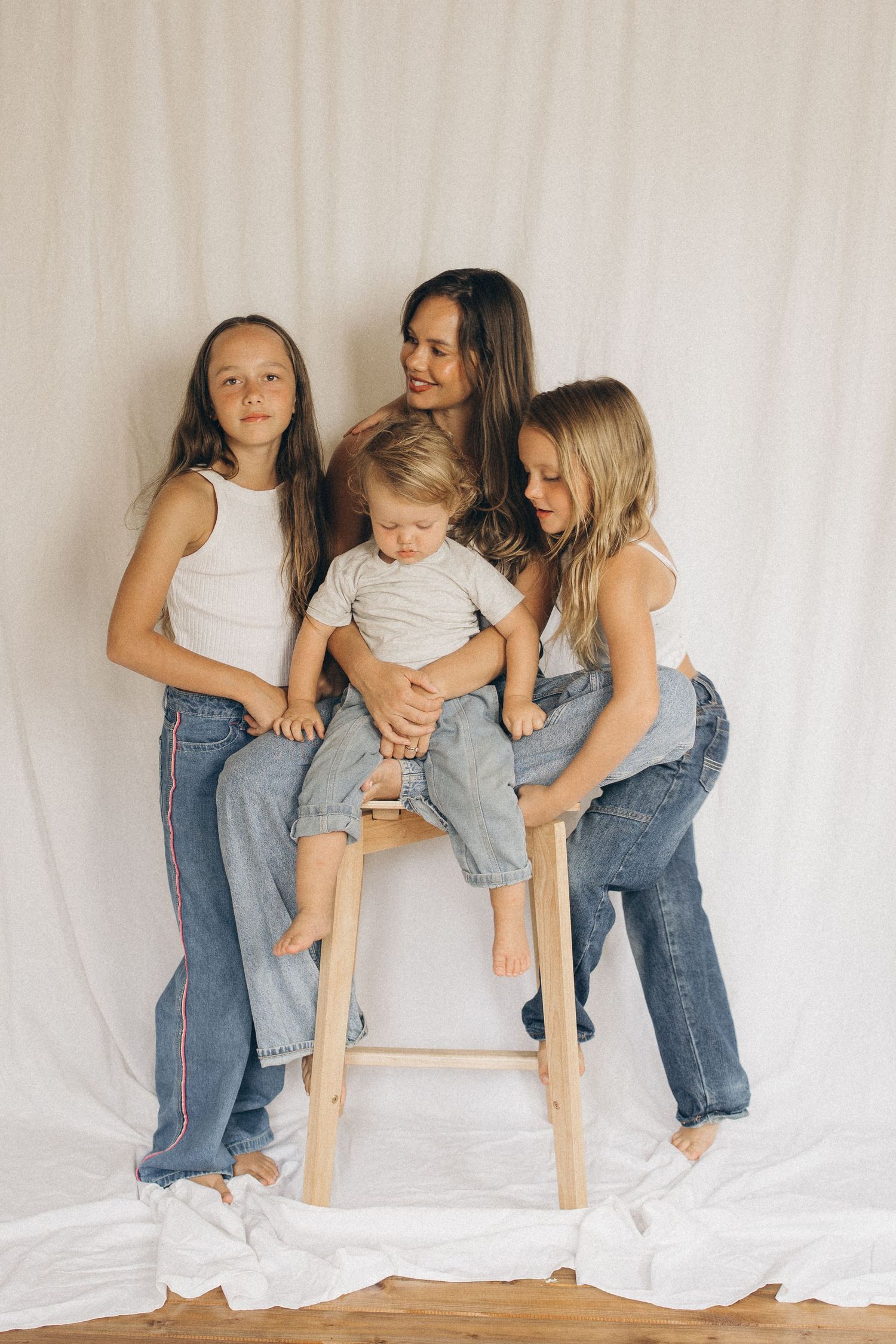 A mother and three children pose together on a wooden stool against a white fabric backdrop in New Zealand.