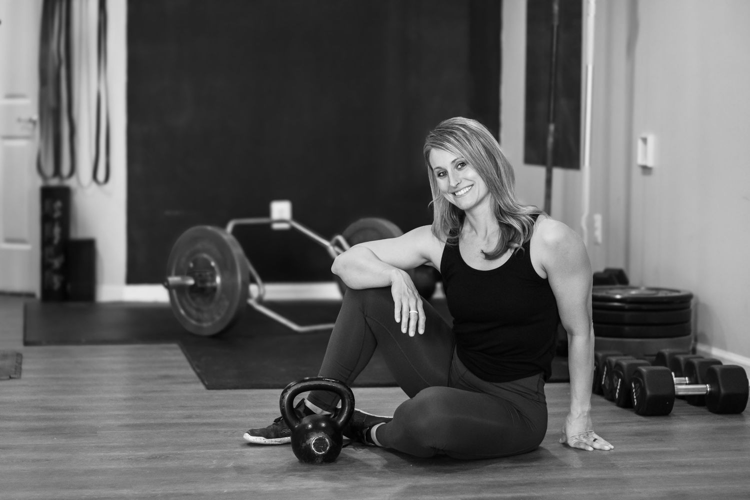 A fitness instructor/ personal trainer takes a break next to a barbell and kettlebell during a branding session in a gym studio.