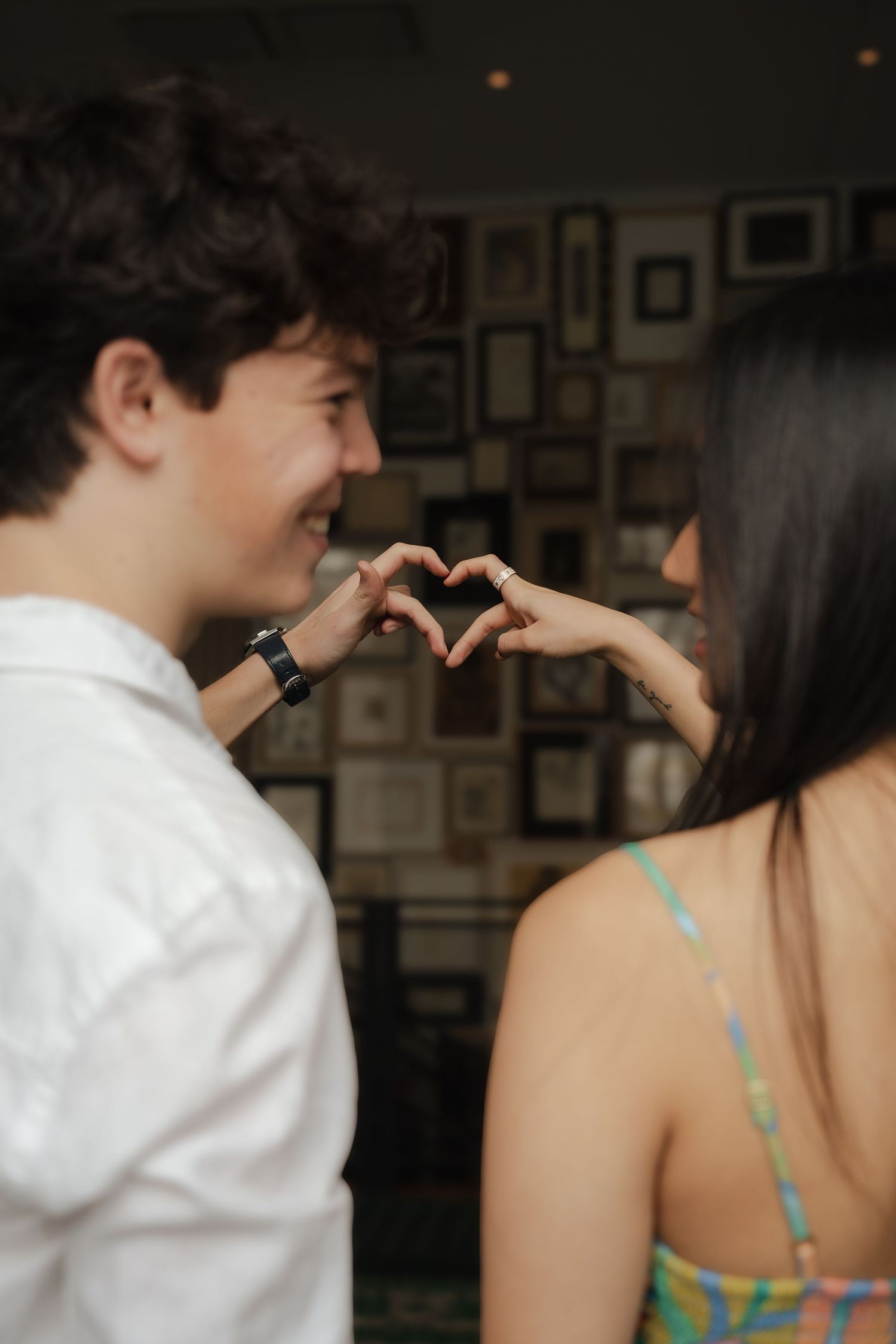 Two people sharing an intimate moment in front of a wall with framed photographs.
