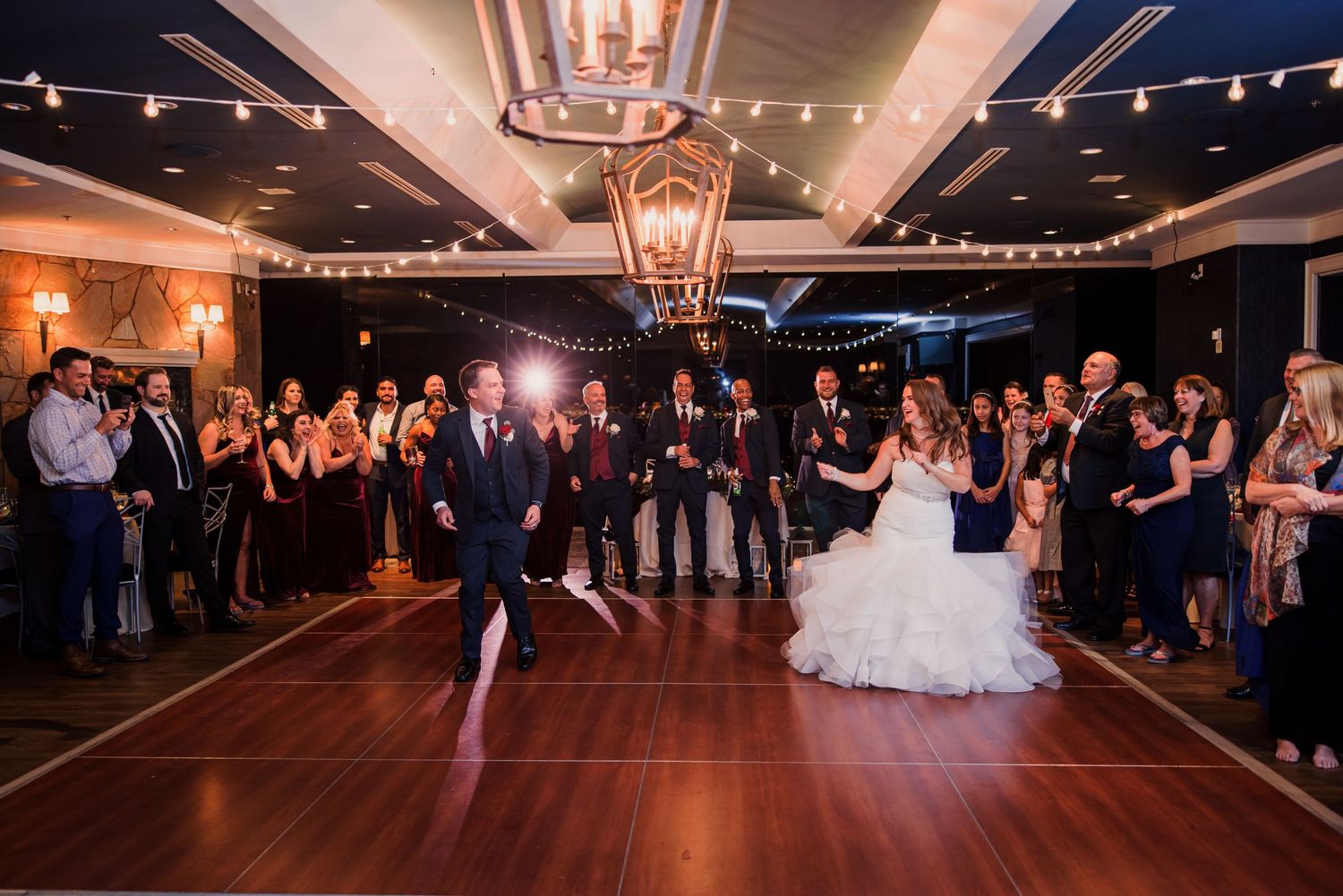Wedding guests gather on a dimly lit dance floor during an evening reception celebration.