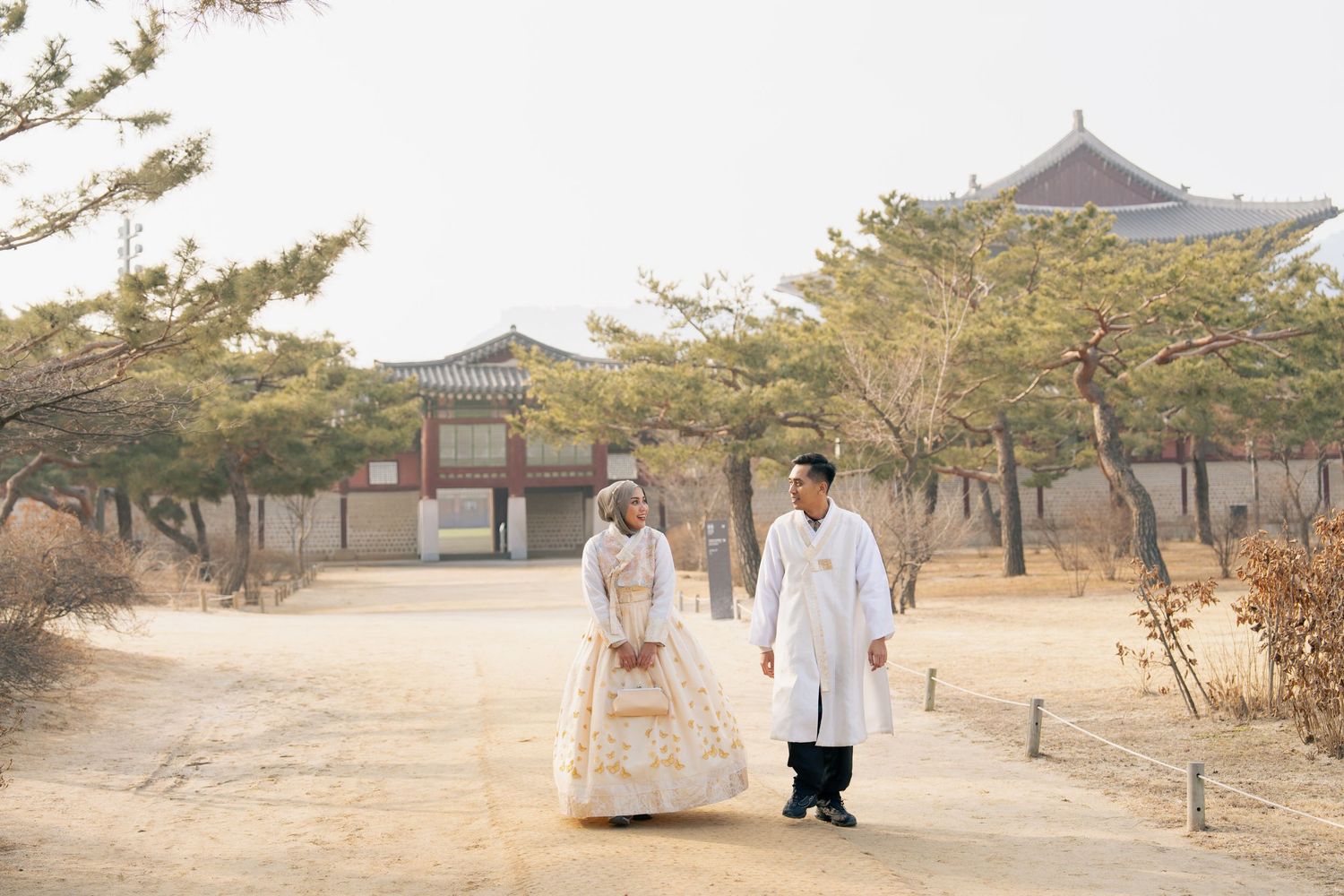 Traditional Korean hanok buildings and walkways surrounded by autumn trees at sunset create a serene cultural landscape.