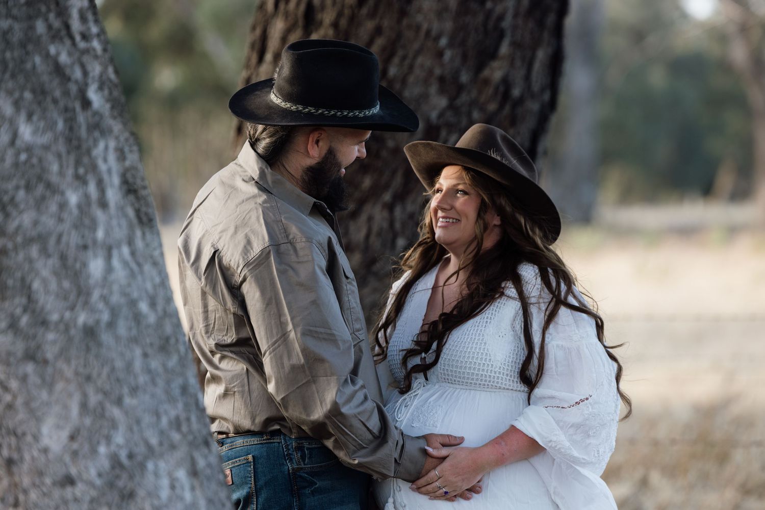 A romantic couple in western attire embraces in a rustic outdoor setting during a photoshoot. location Benalla