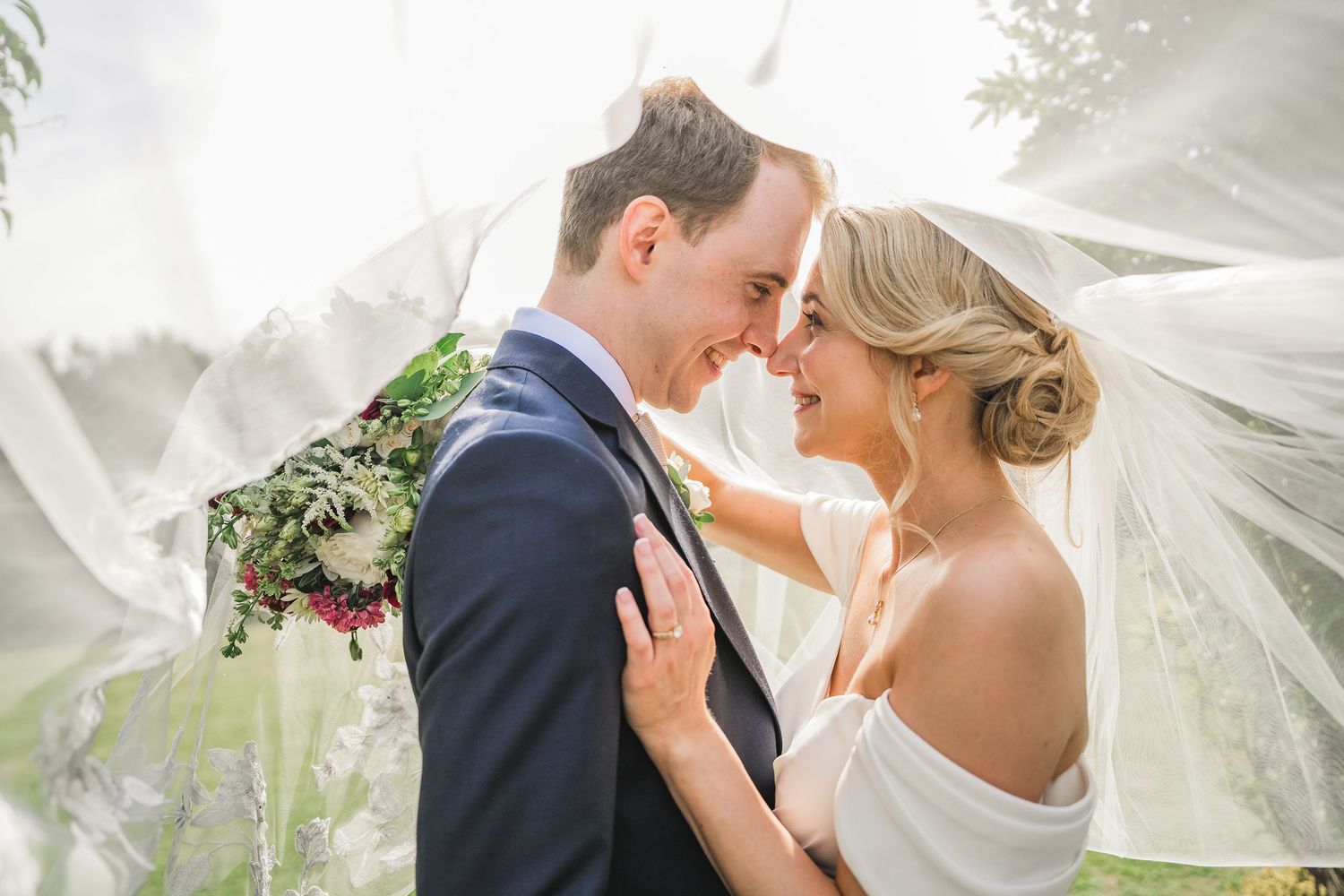 A beautifully caught, intimate moment for this handsome couple. The bride has her hair in a low, curled chignon bun. Soft, dewy makeup.