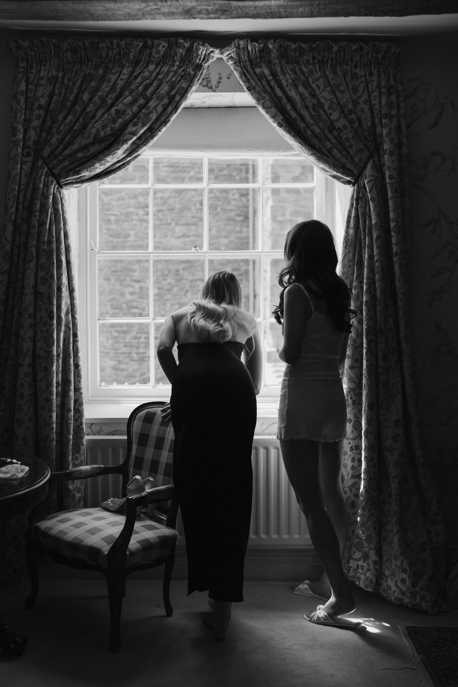 bride and friend sneaking a peak out the window at dewsall court in Herefordshire