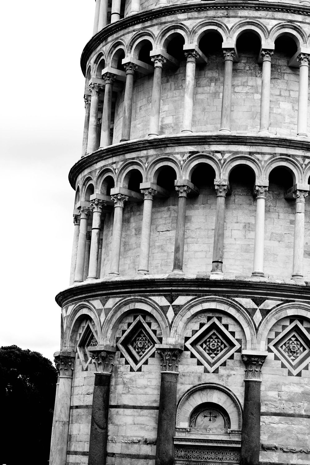 Black and white architectural detail of the Leaning Tower of Pisa showing ornate arches and columns.