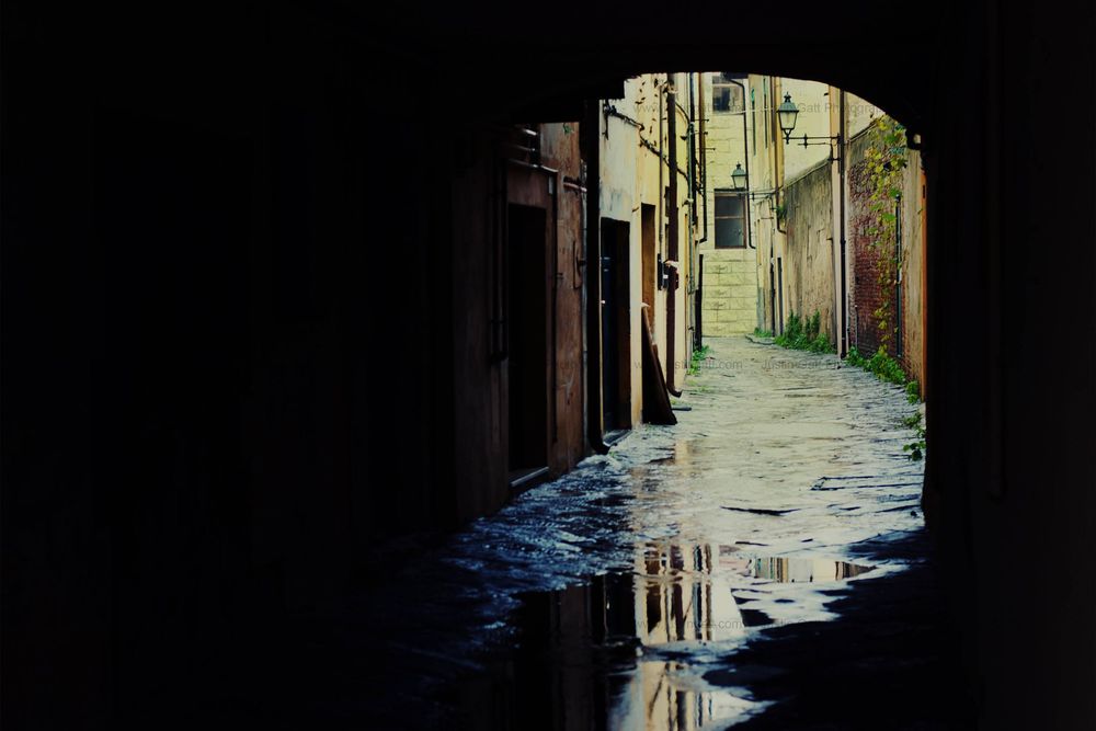 Reflective puddle in a narrow Italian alleyway creating mirror effect under an archway.