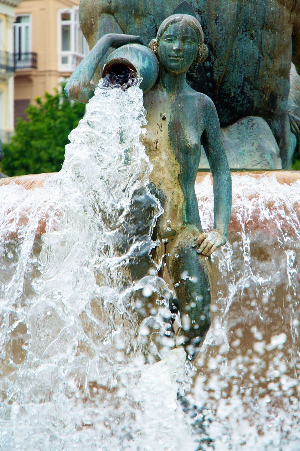Bronze fountain statue with water spraying dramatically in an urban park setting.