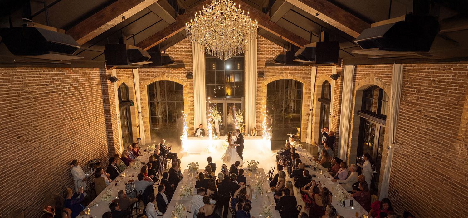 Aerial view of elegant wedding reception in rustic brick venue with chandelier lighting.