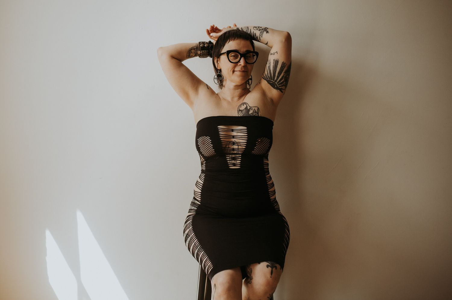 A figure poses in black lingerie against a beige wall, creating a series of artistic boudoir portraits.