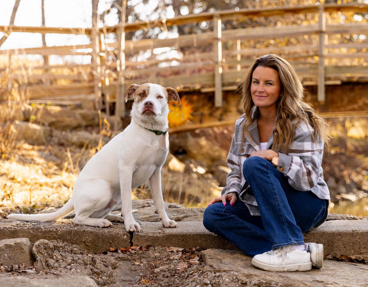 A white dog rests on stone steps during a golden hour photoshoot in an outdoor setting.