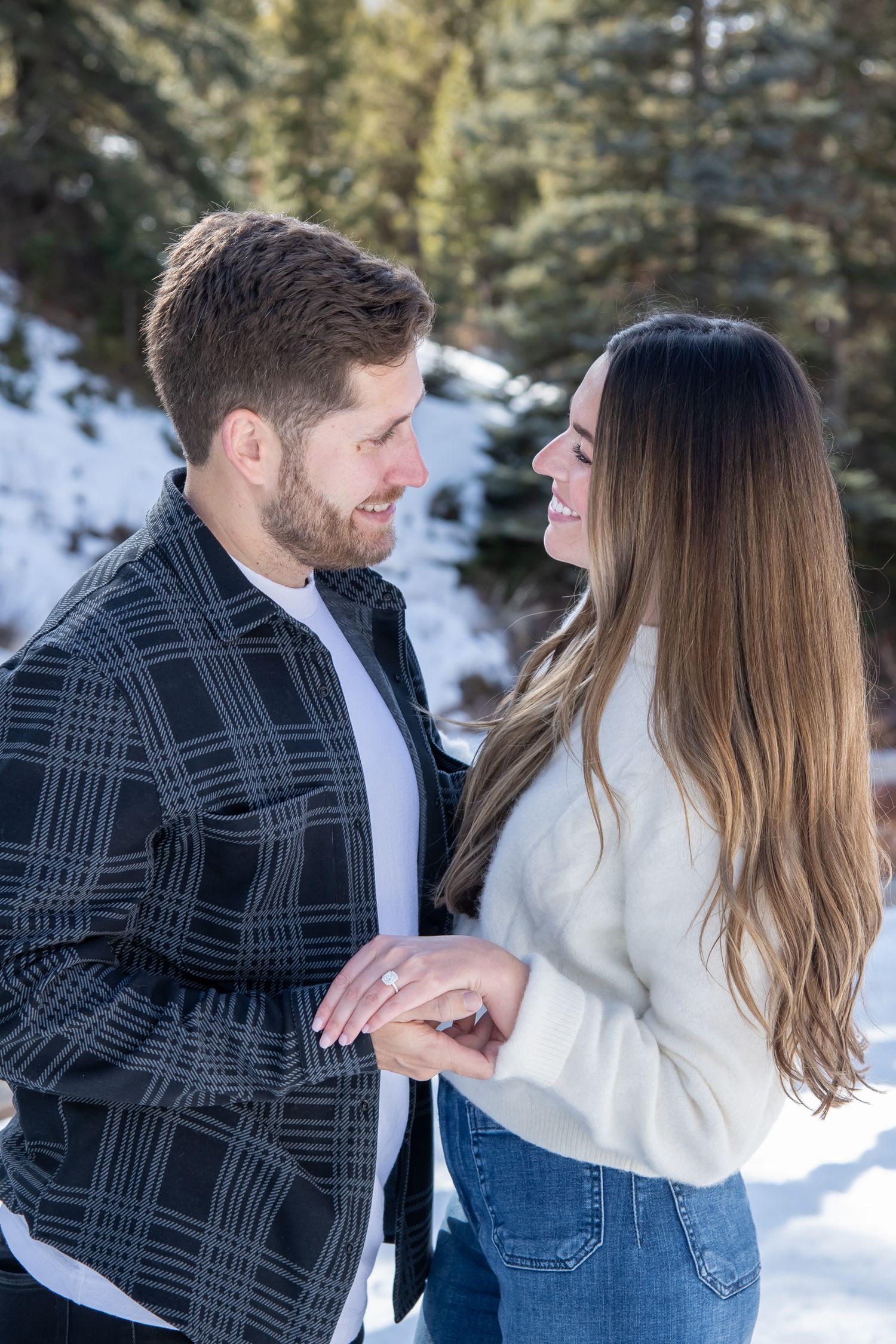 A cute couples looks at each other and hold hands during their winter engagement photo session in Vail Colorado after a surprise proposal
