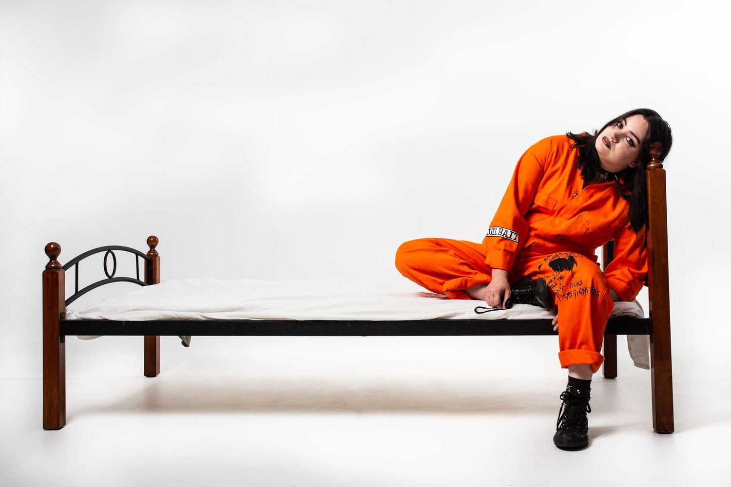 Person in bright orange jumpsuit performing acrobatic moves and poses on a low platform against white background.