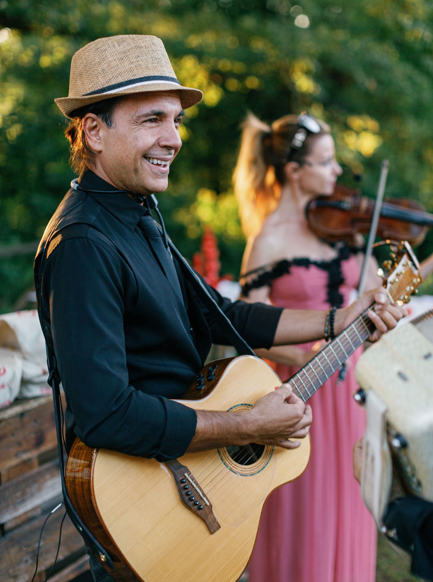 Musicians perform with acoustic guitars and violin at an outdoor event in natural lighting.