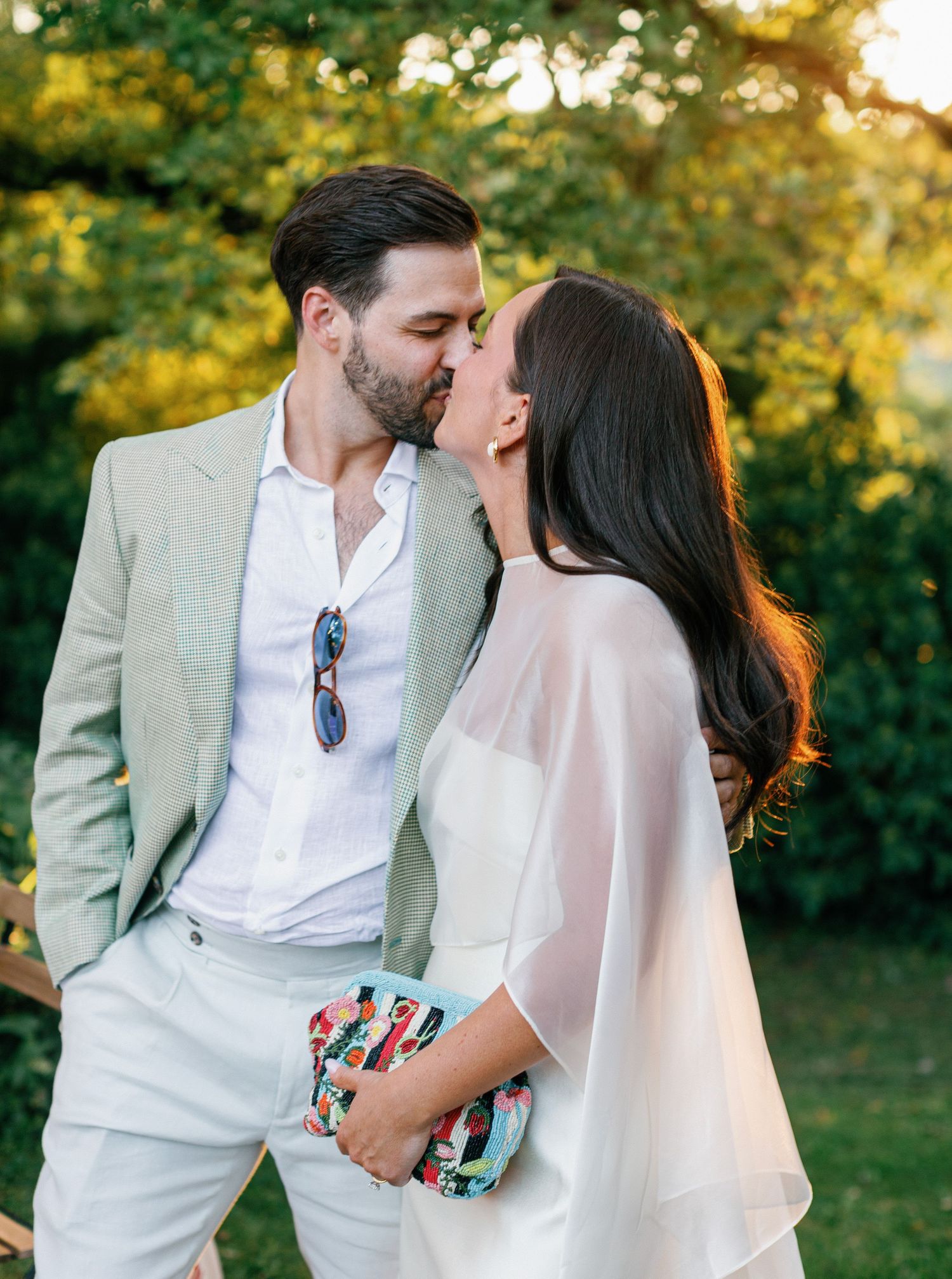 A romantic couple sharing a tender kiss outdoors during golden hour in a garden setting.