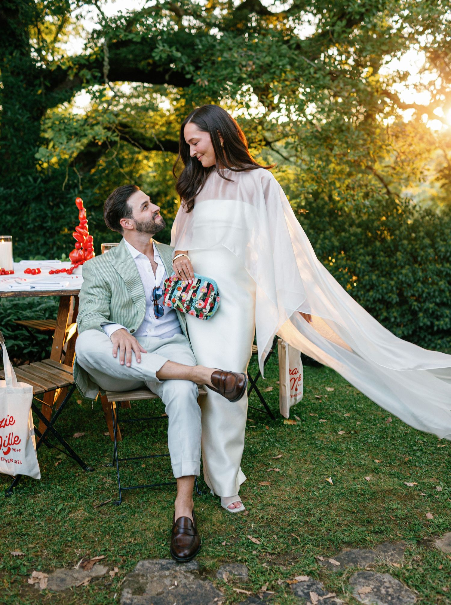 A romantic outdoor wedding scene with flowing white dress and greenery at sunset in a garden setting.