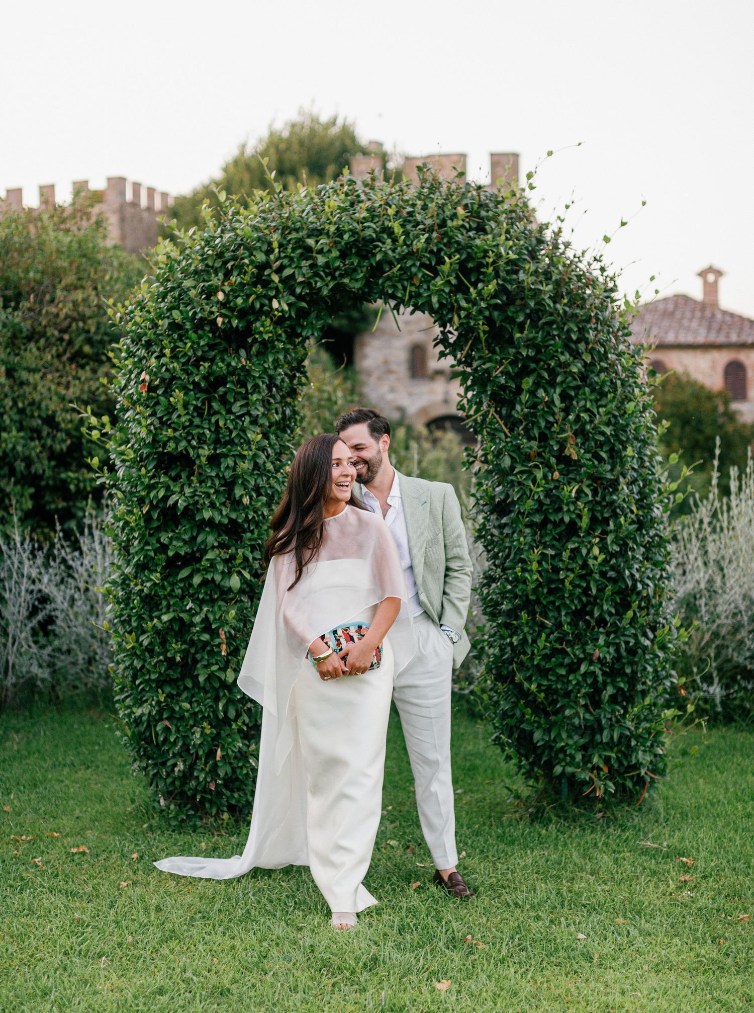 A romantic couple shares a playful dip pose in front of lush green hedges during their wedding photo session.