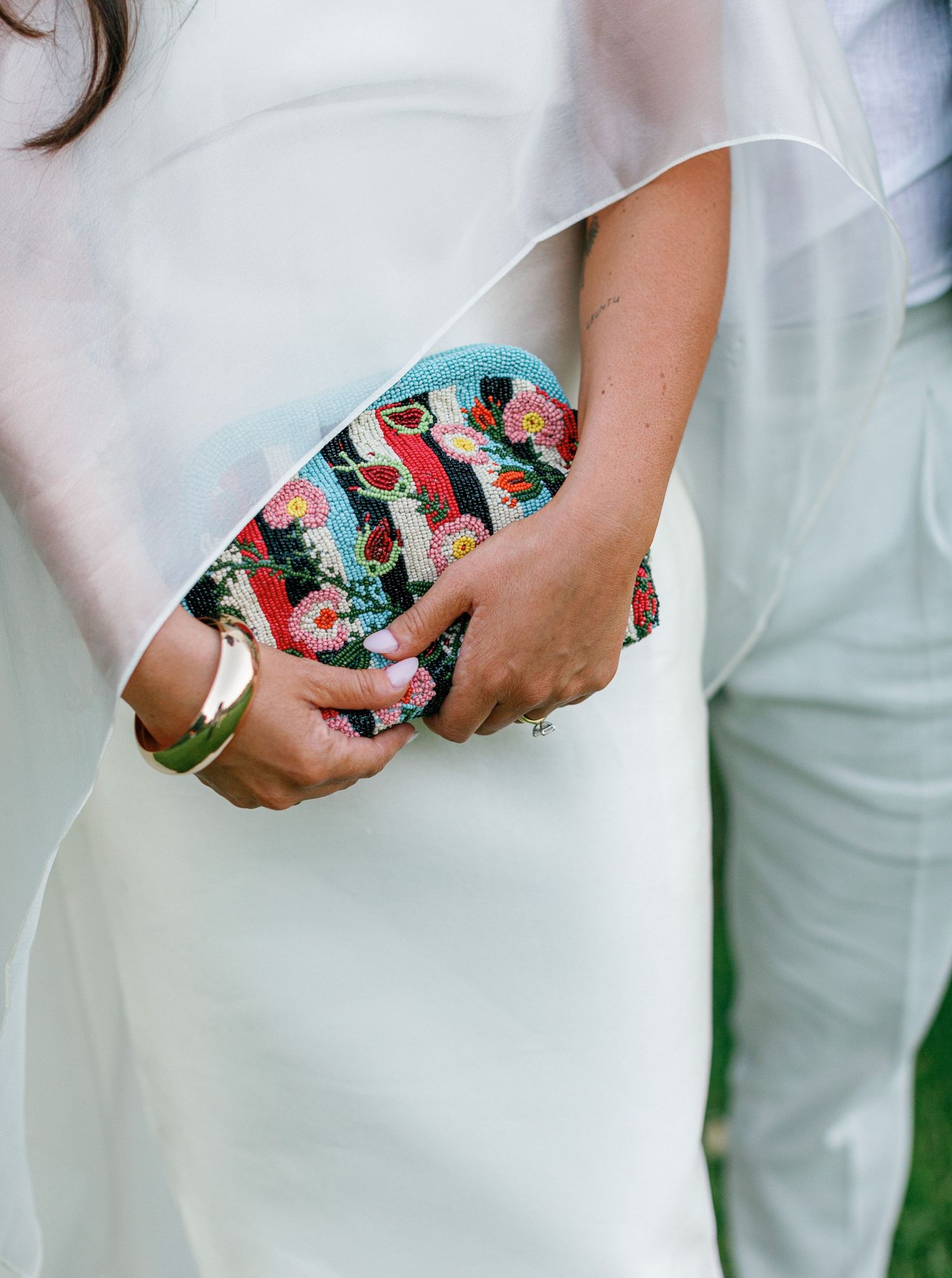 Hands holding a colorful butterfly-patterned clutch purse against a white dress background.