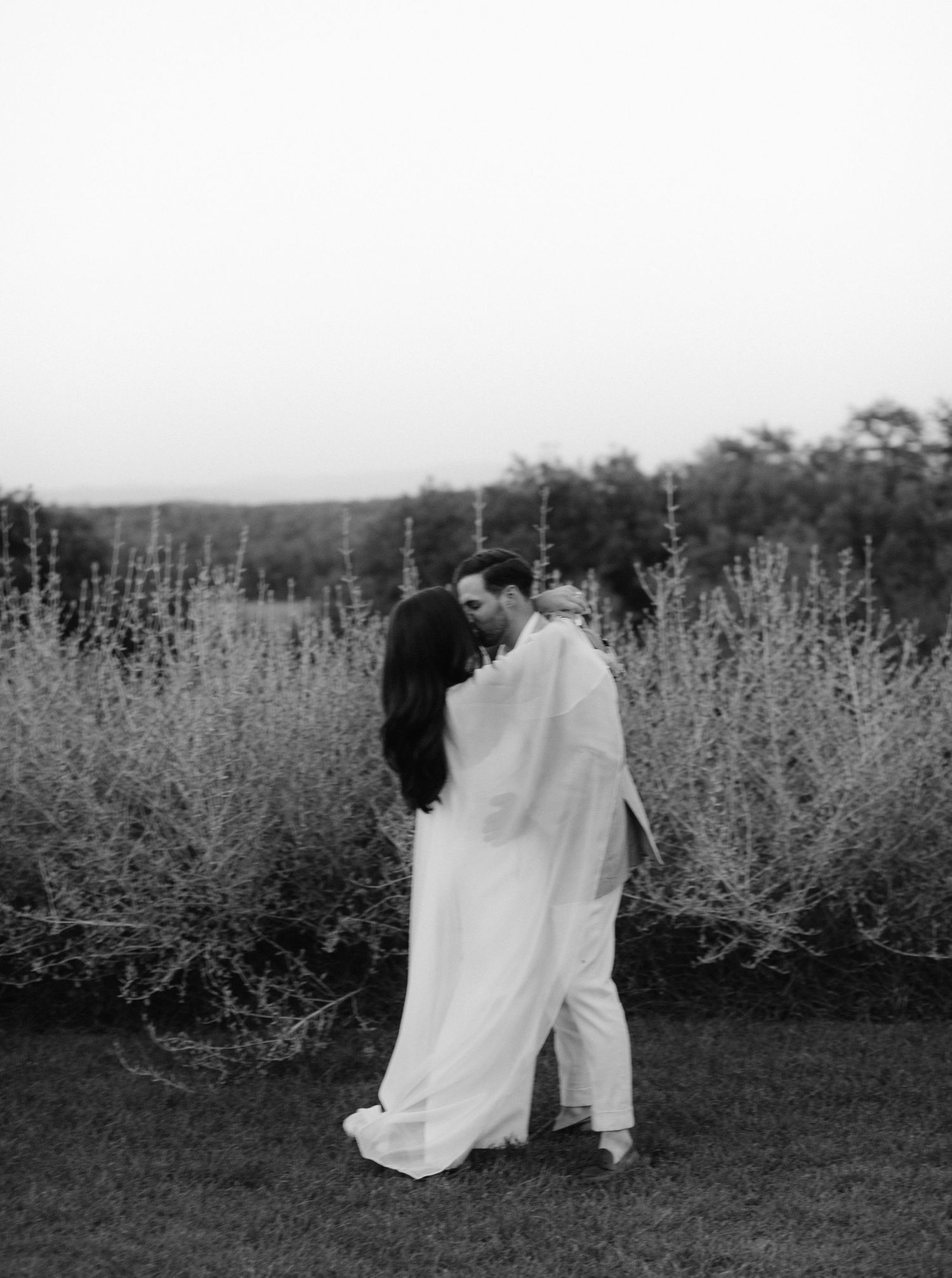 A series of black and white photos showing a couple in wedding attire walking through a field of tall flowers.