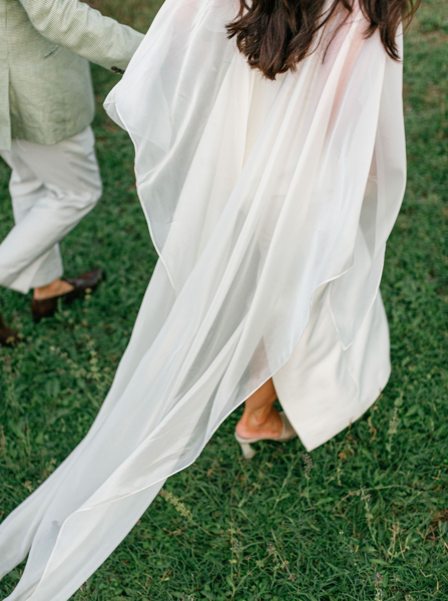 Flowing white wedding dress fabric and bare feet walking on green grass with ethereal movement.