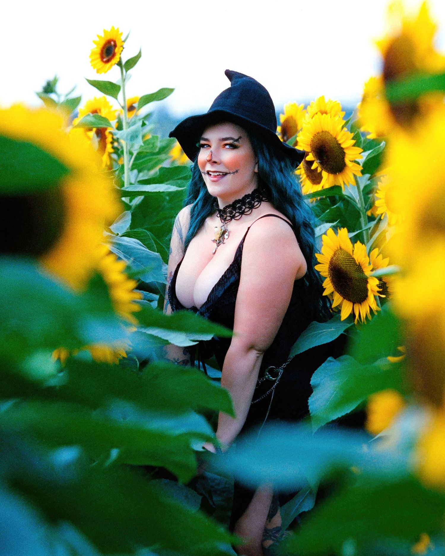 David G Holt Photography - Woman in black hat posing playfully among bright yellow sunflowers in a summer field.