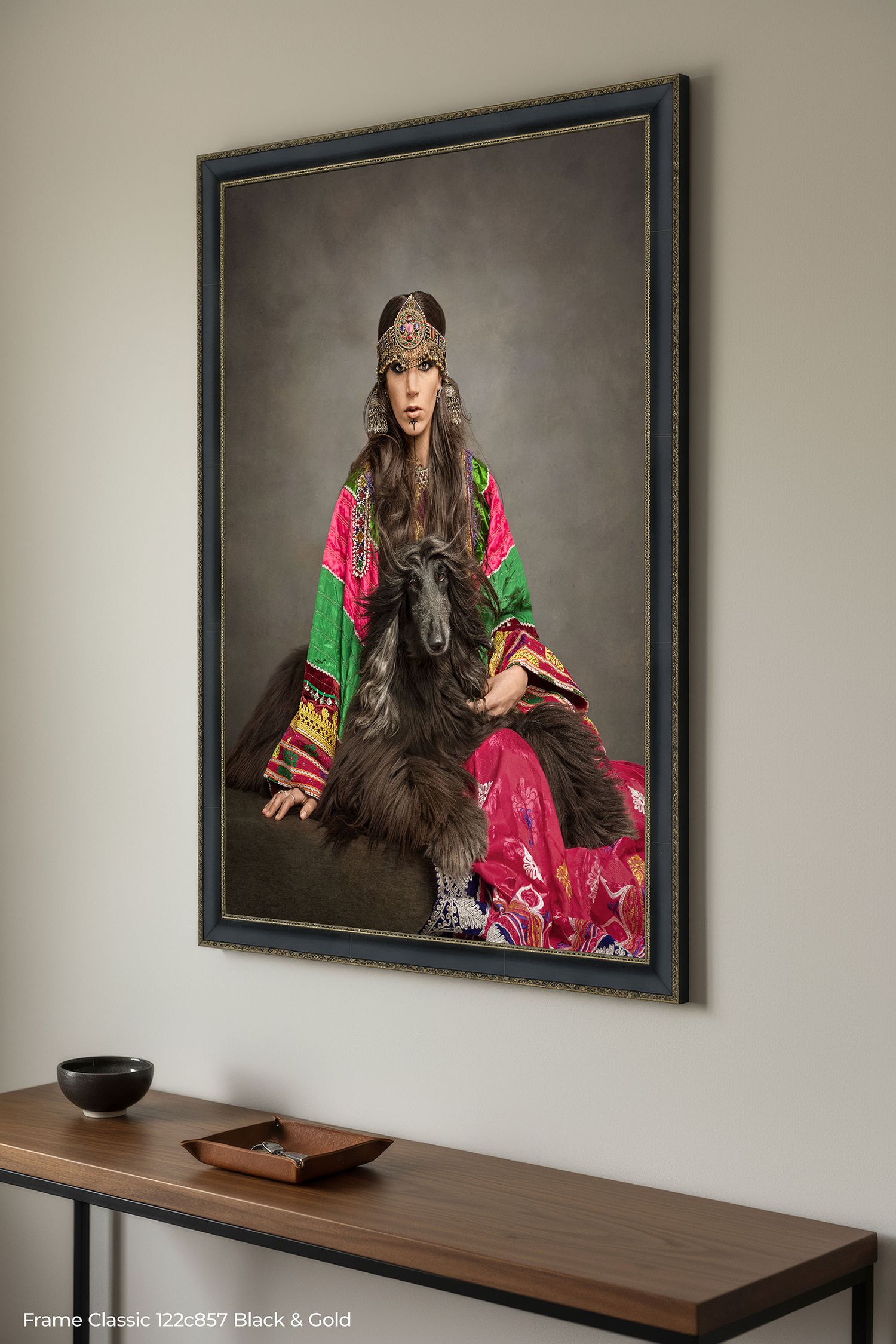 A framed portrait of someone in ornate traditional dress with vibrant pink and green fabrics hangs above a wooden shelf.