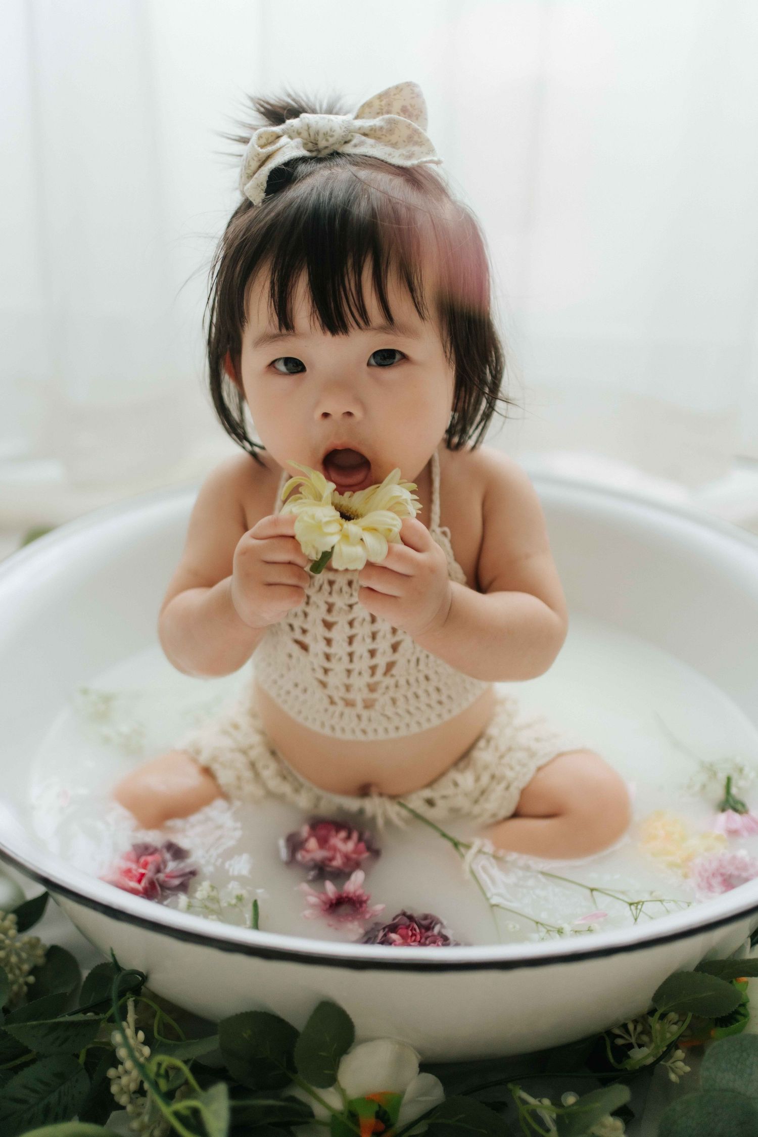 Baby in white outfit plays with colorful pastel balloons and smash cake during first birthday photoshoot.