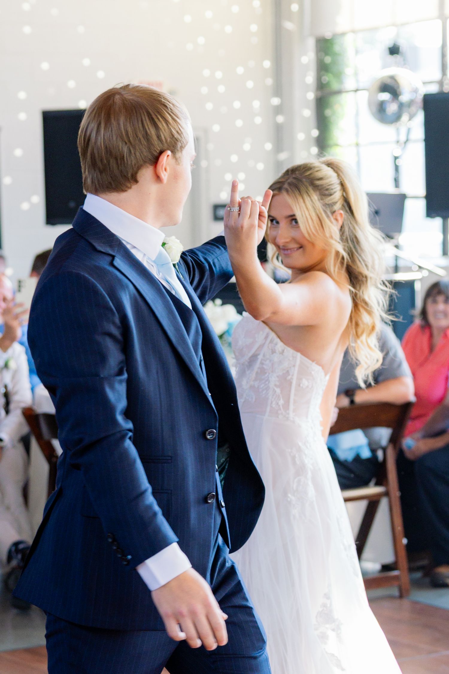 A couple shares their first dance at a wedding reception, with the bride in white and groom in navy suit.