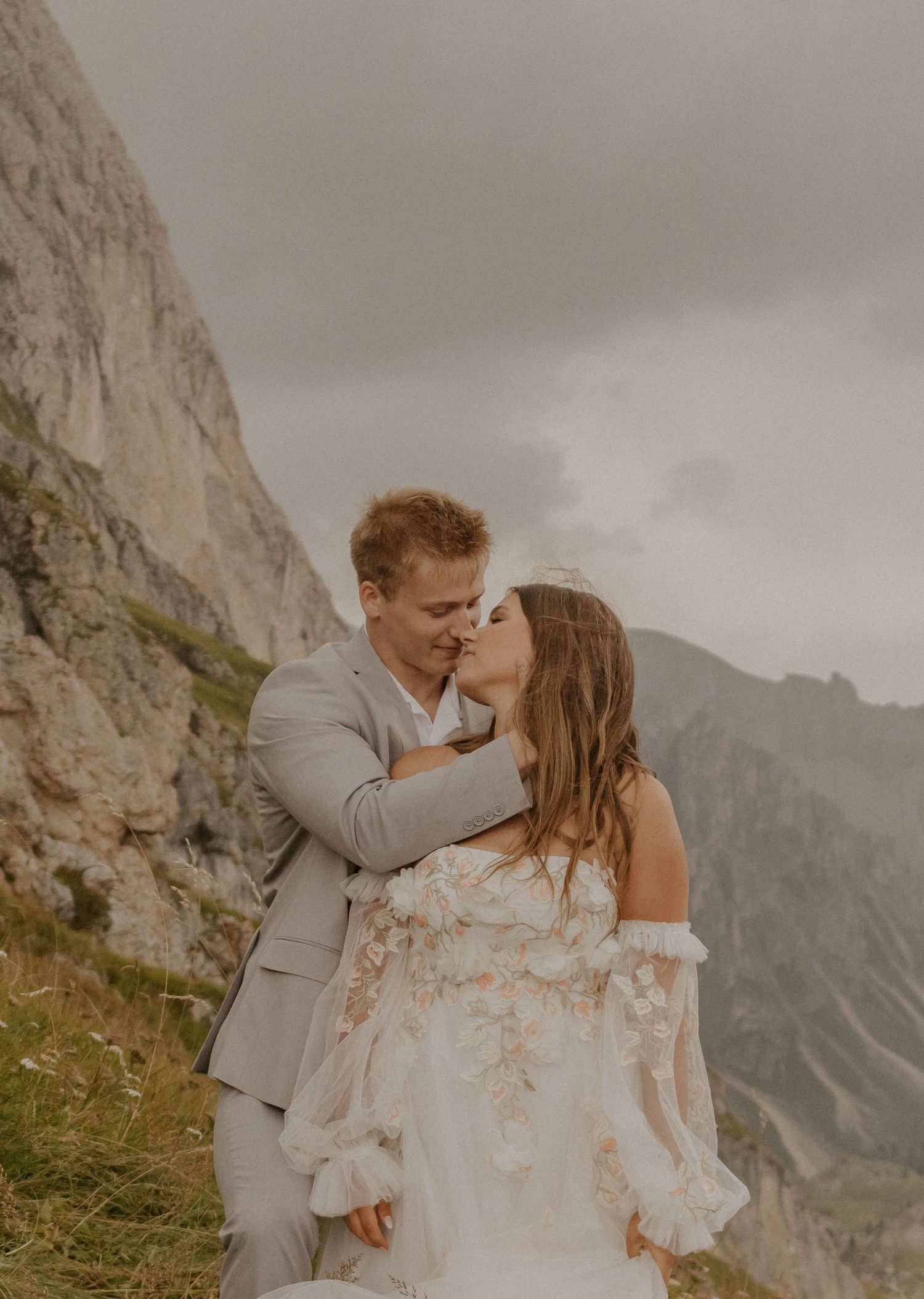 A couple shares an intimate kiss against a backdrop of dramatic mountain peaks in the Dolomites.