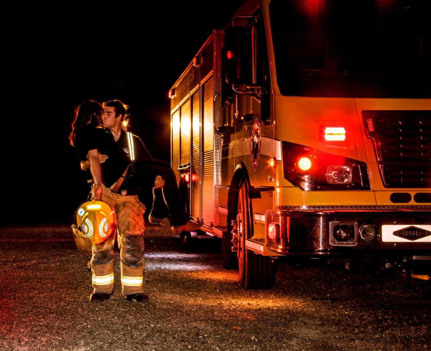A firefighter stands beside an illuminated fire truck at night with reflective gear visible.
