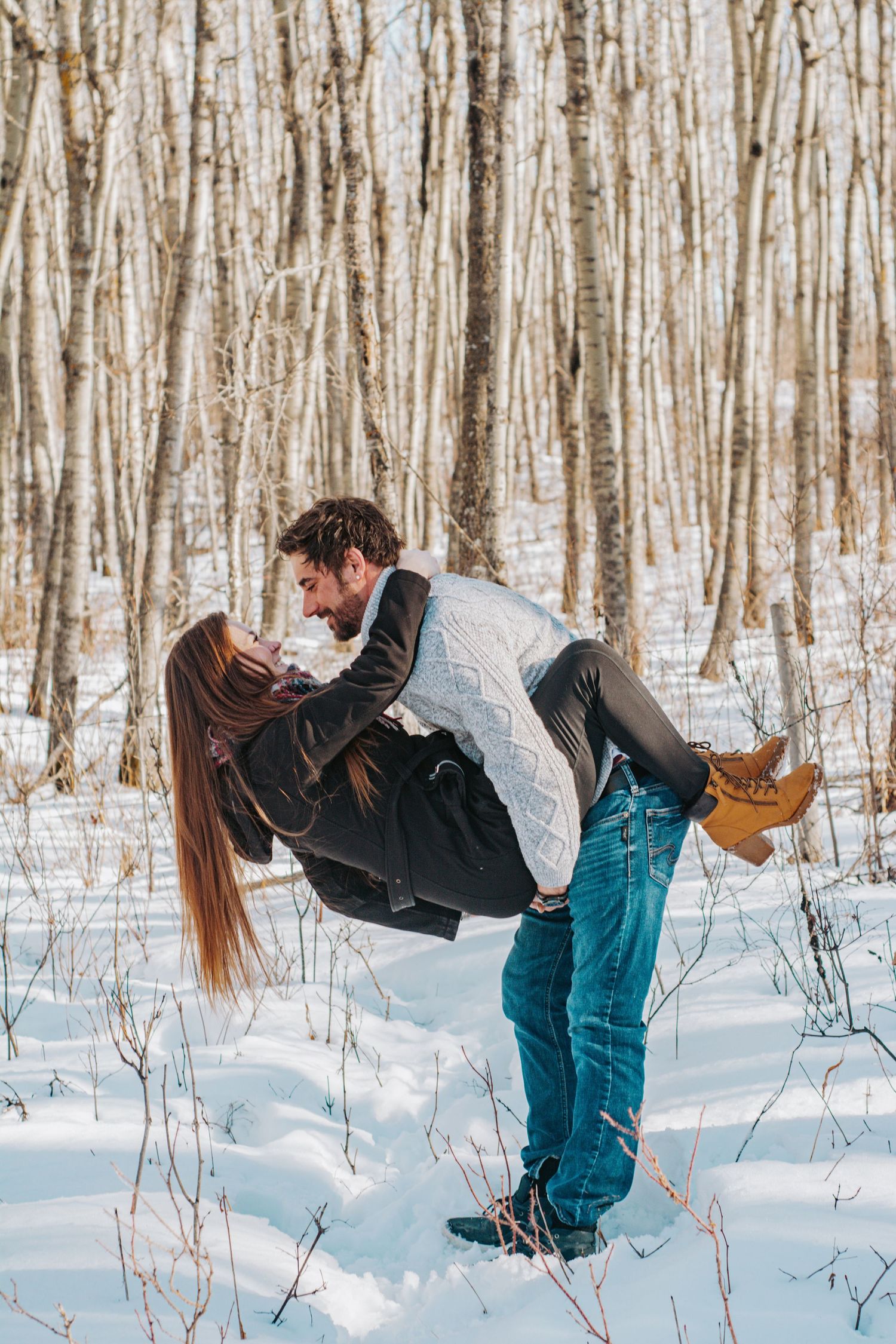 A romantic winter scene shows a couple embracing in a snowy forest with bare trees in the background.