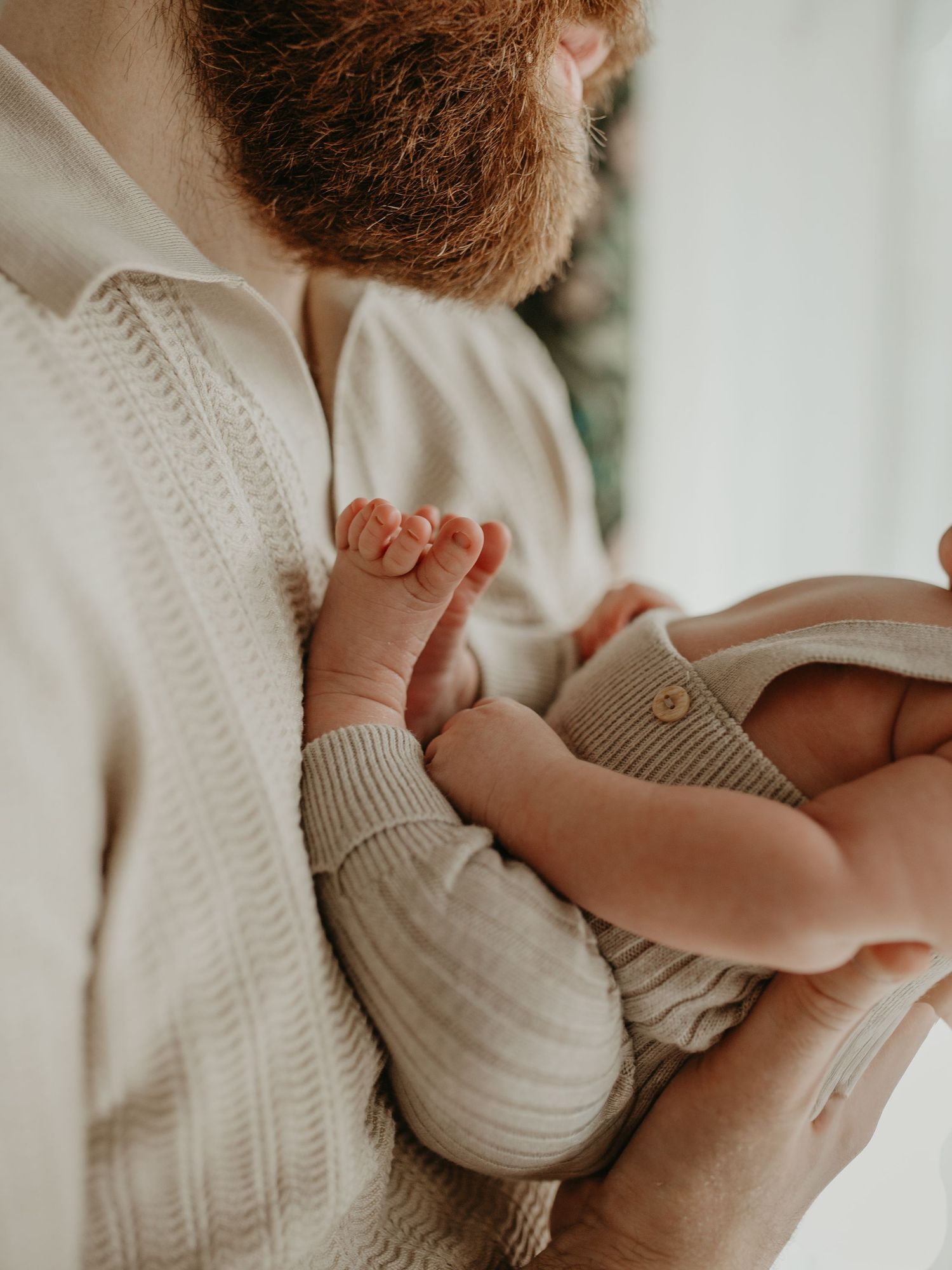 A tender moment captured in soft beige tones as a baby in a knit sweater nurses in gentle natural light.