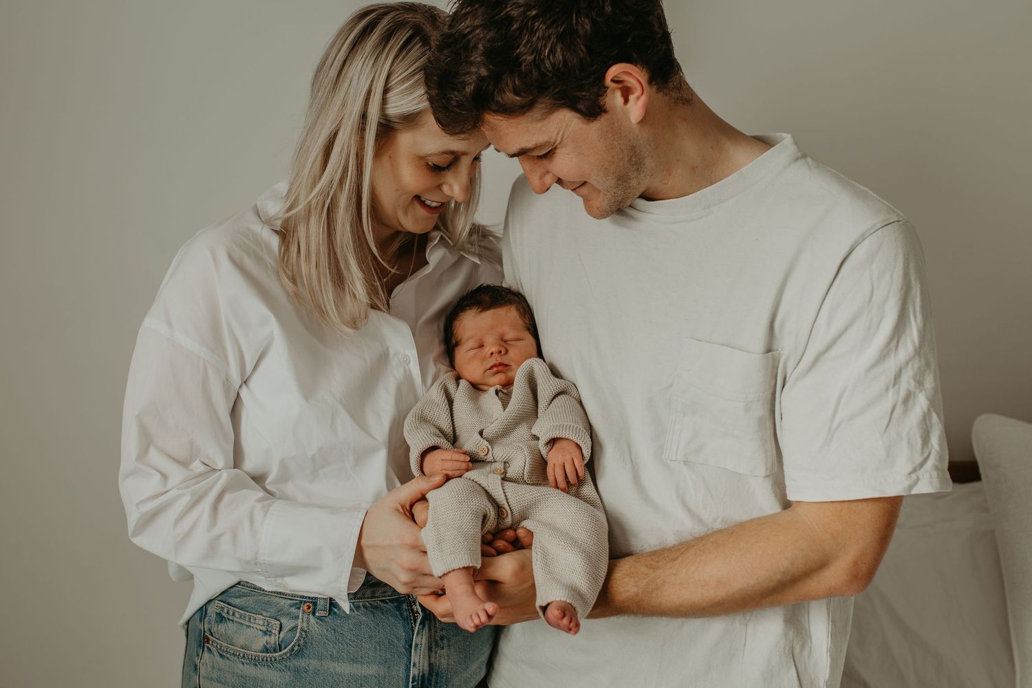 A tender moment as parents gaze lovingly at their sleeping newborn baby in warm lighting.