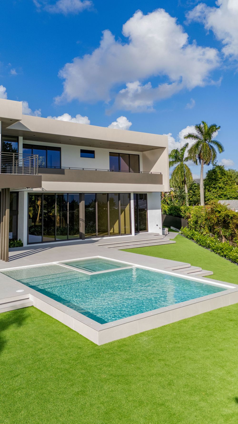 Modern luxury villa with geometric architecture and infinity pool set in a manicured lawn under blue skies.