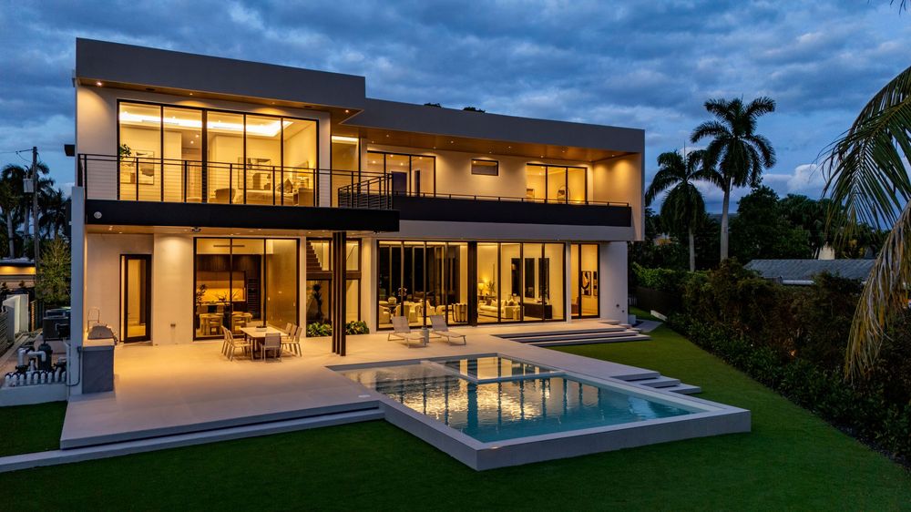 Contemporary white house exterior with floor-to-ceiling windows and warm interior lighting at dusk.