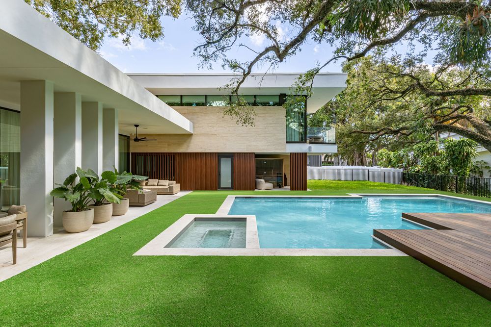 Expansive backyard featuring a geometric swimming pool surrounded by manicured lawn and tropical landscaping.