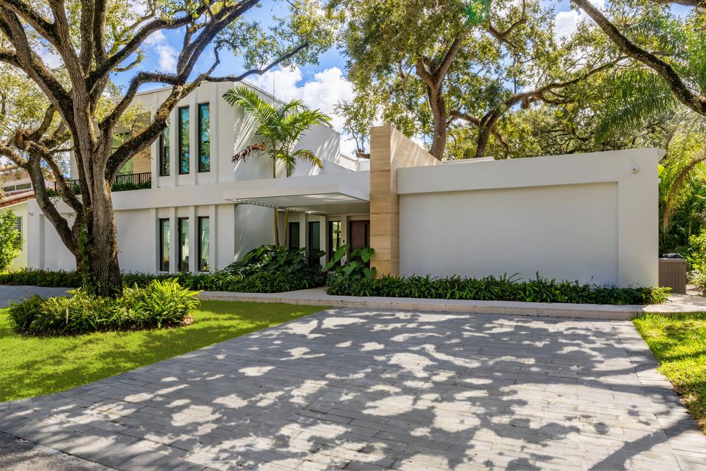 Sweeping driveway entrance to a contemporary white mansion with tropical landscaping.