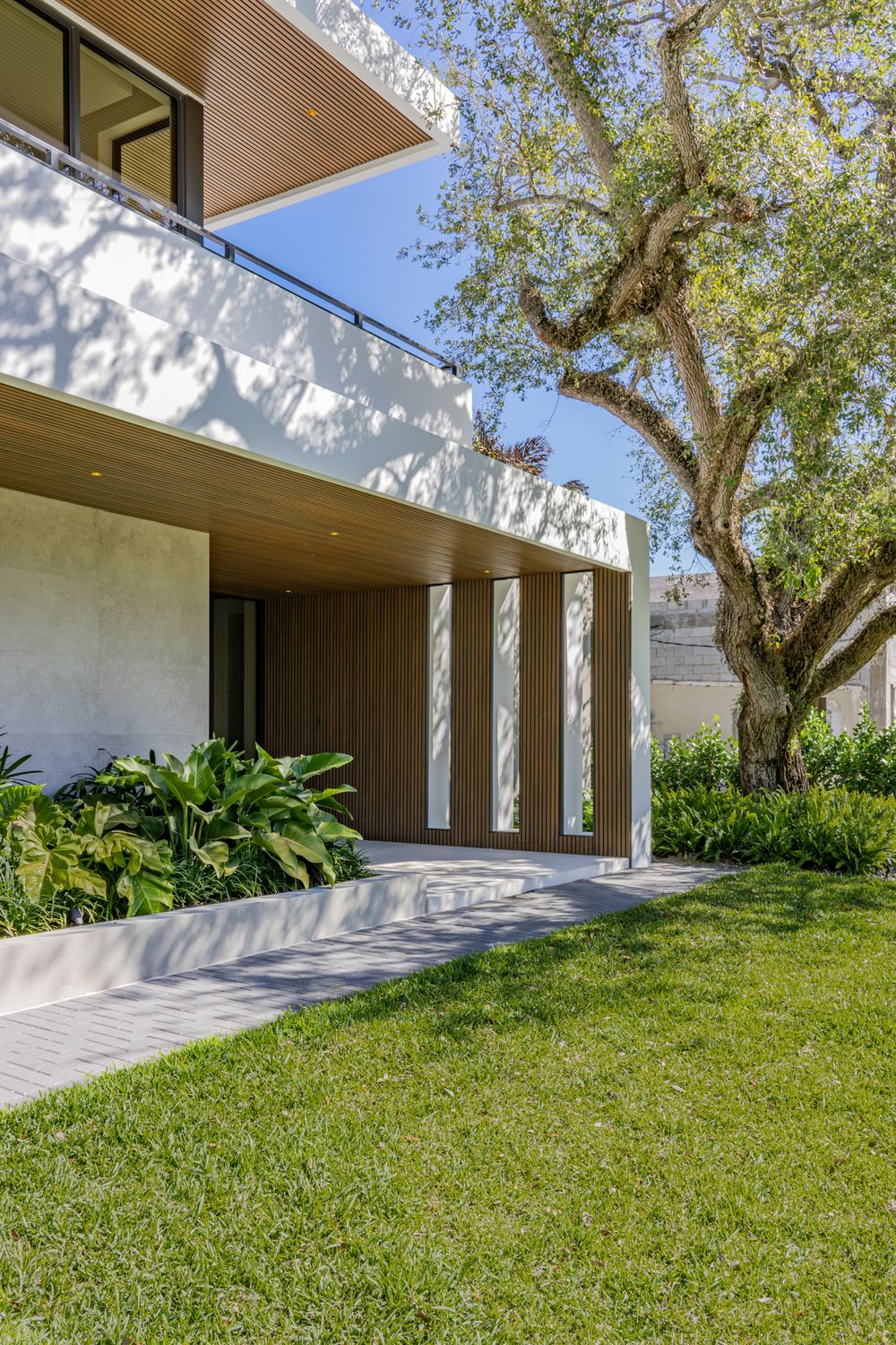 Landscaped yard featuring mature trees and tropical plants alongside a modern white architectural structure.